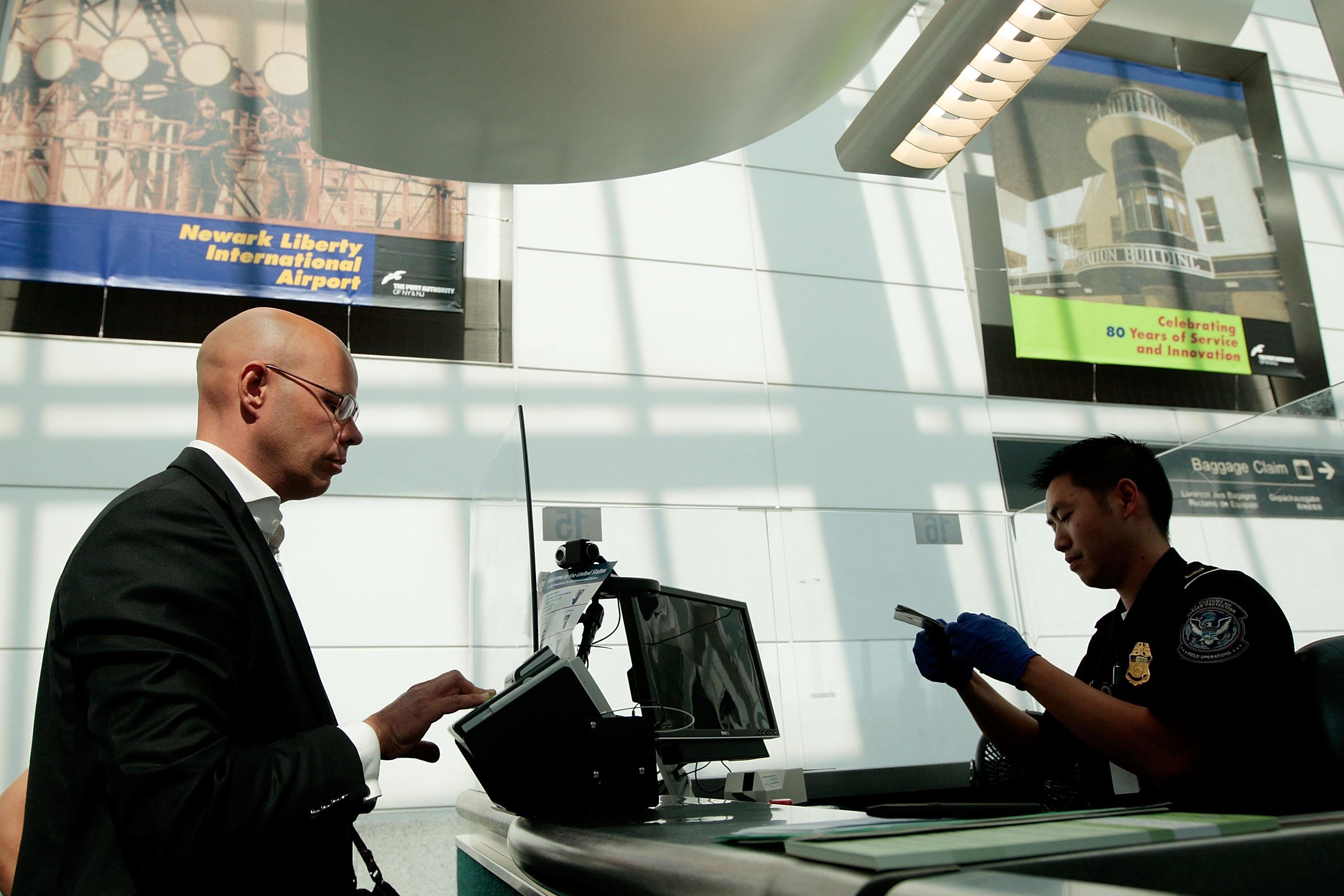 A traveler stands beside a desk as a TSA official examines his passport.
