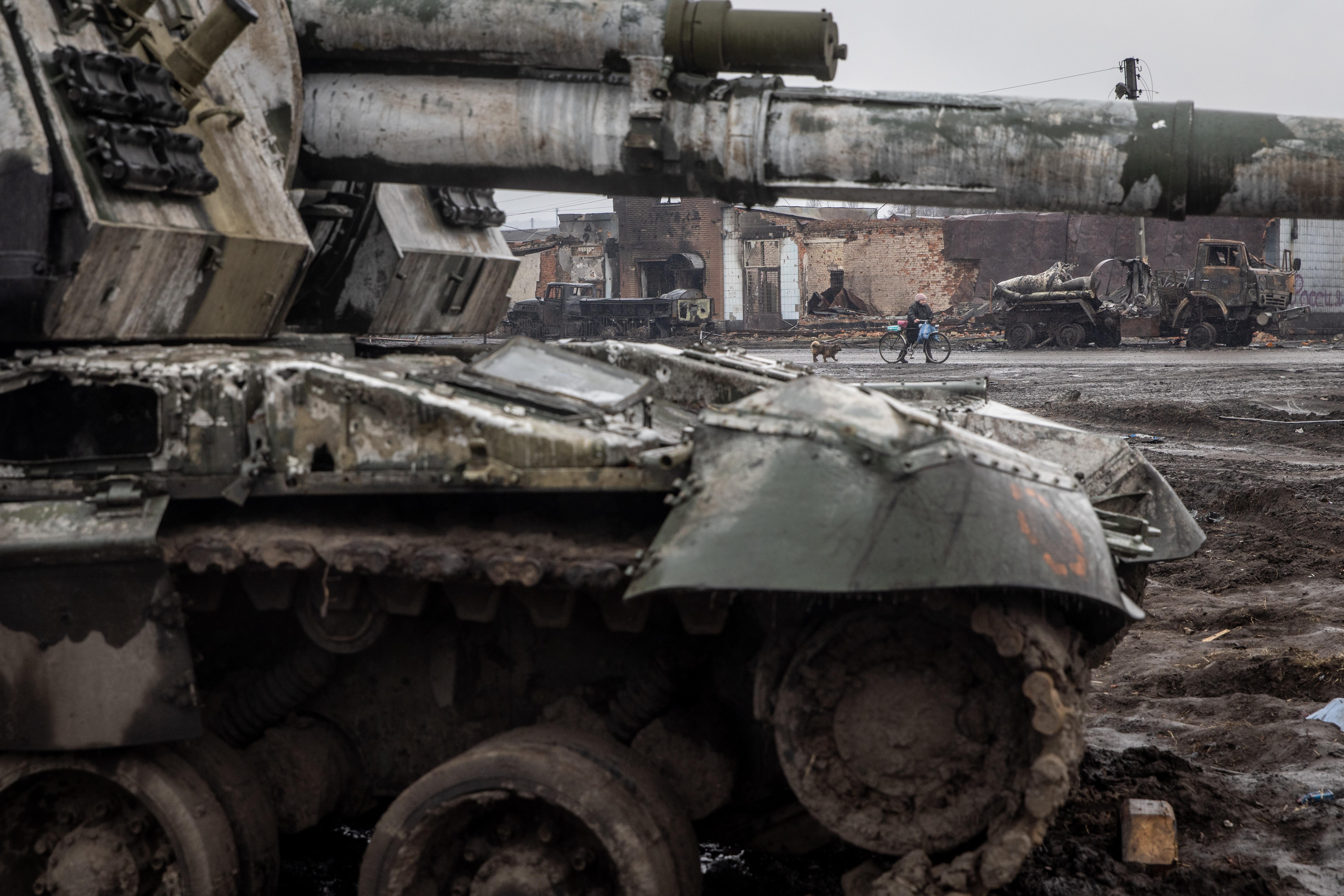 A woman and her dog walk past a destroyed Russian tank