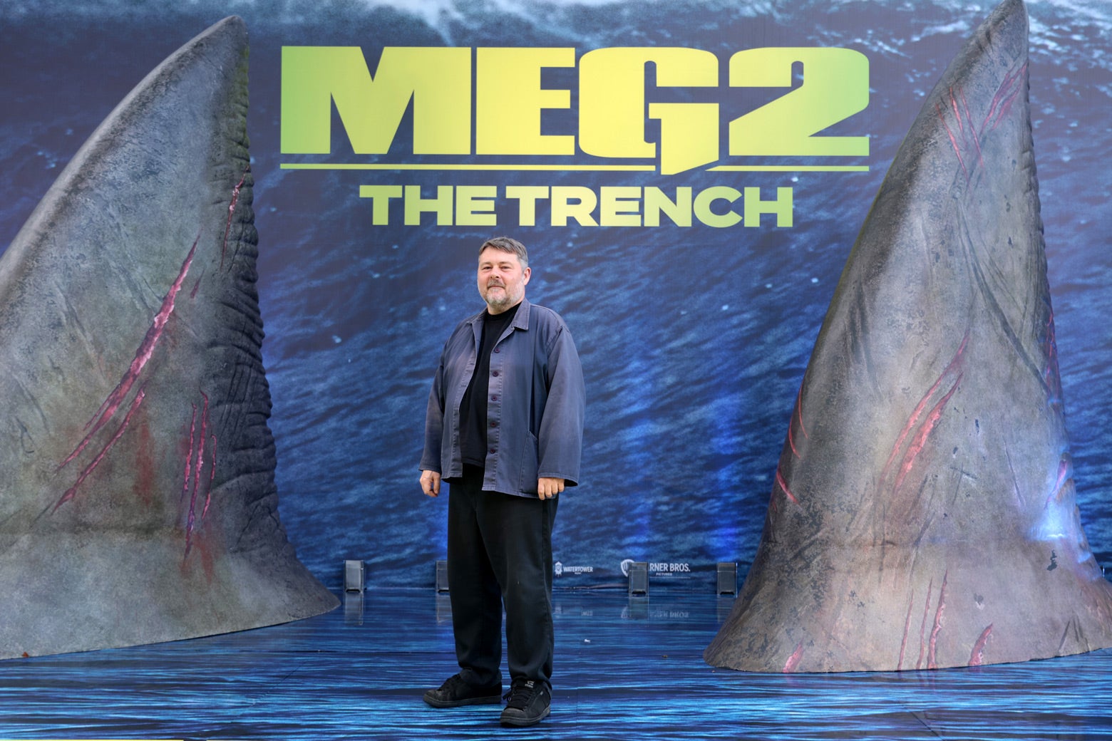 Wheatley smiles halfheartedly from between huge novelty shark fins at the opening of The Meg 2. 