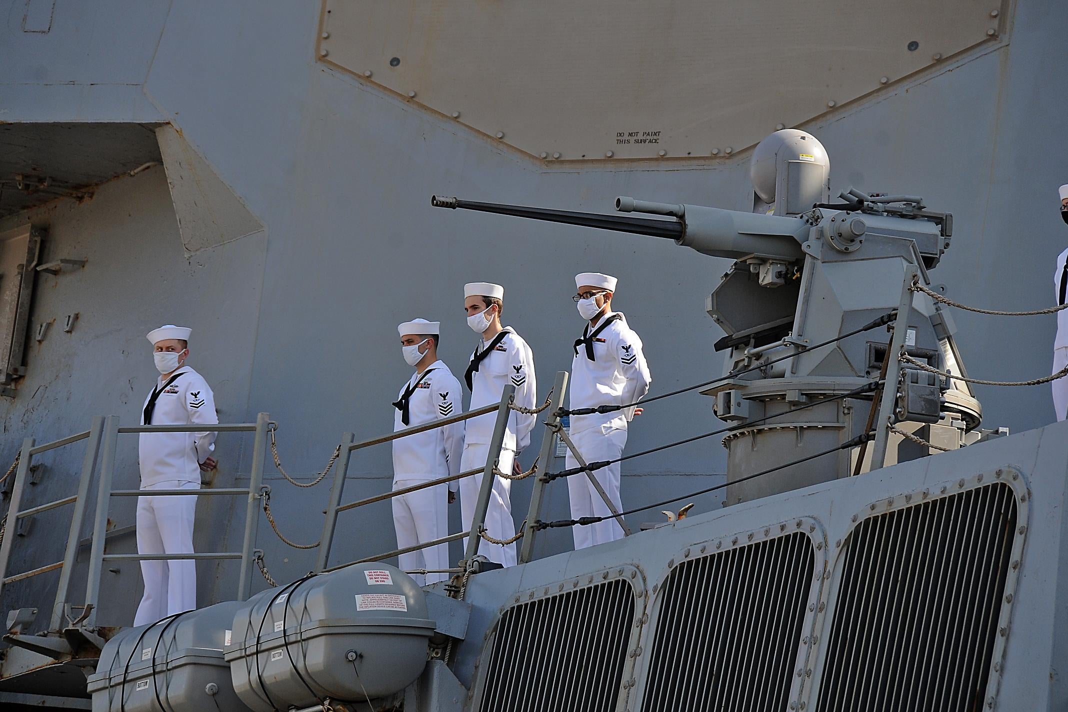 Sailors wearing masks stand on a guided-missile destroyer.