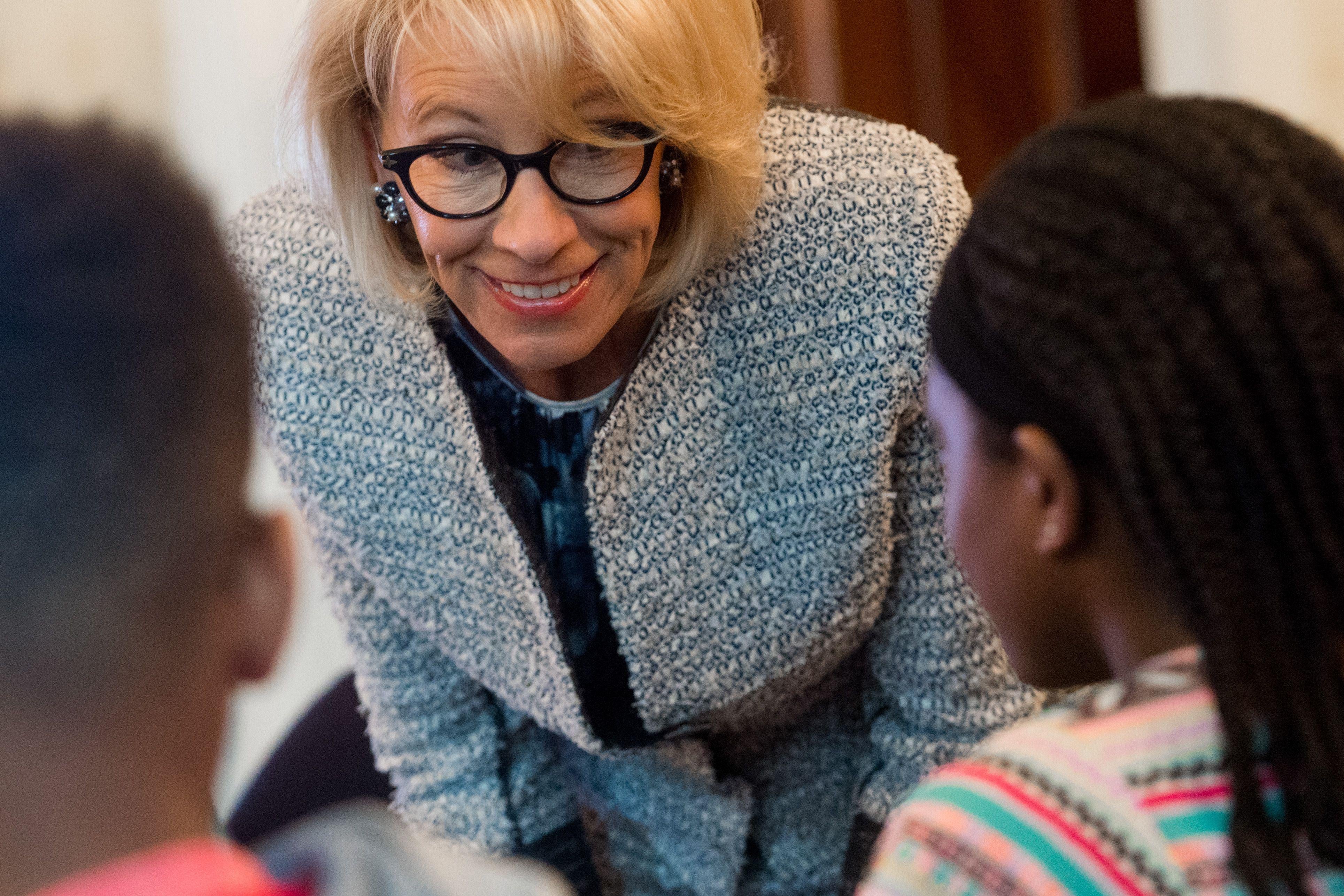 Betsy DeVos bends over and smiles at kids.