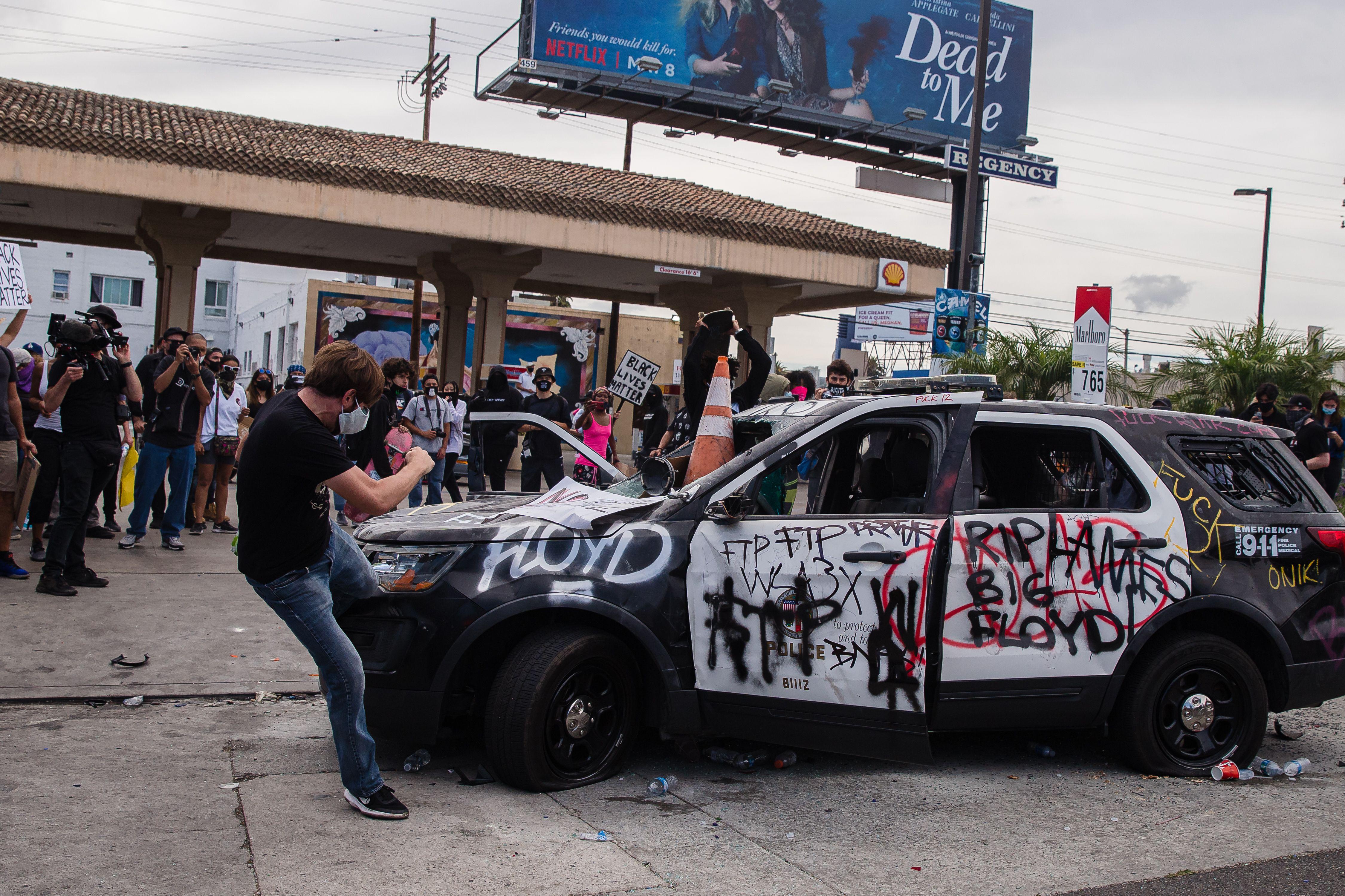 A demonstrator kicks a damaged police vehicle in Los Angeles on May 30, 2020.