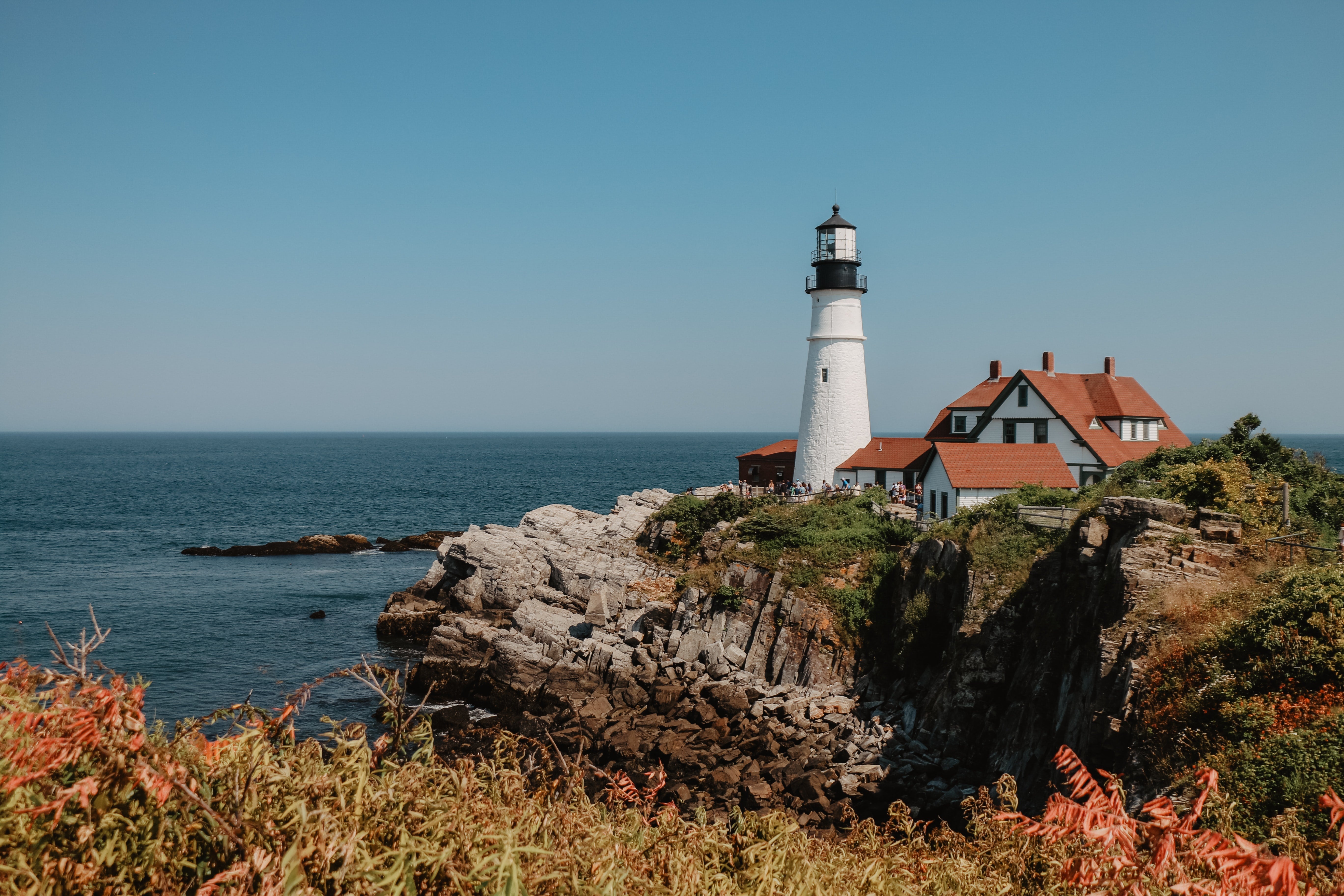 A lighthouse and small house on the edge of a cliff on the ocean in Portland, Maine.
