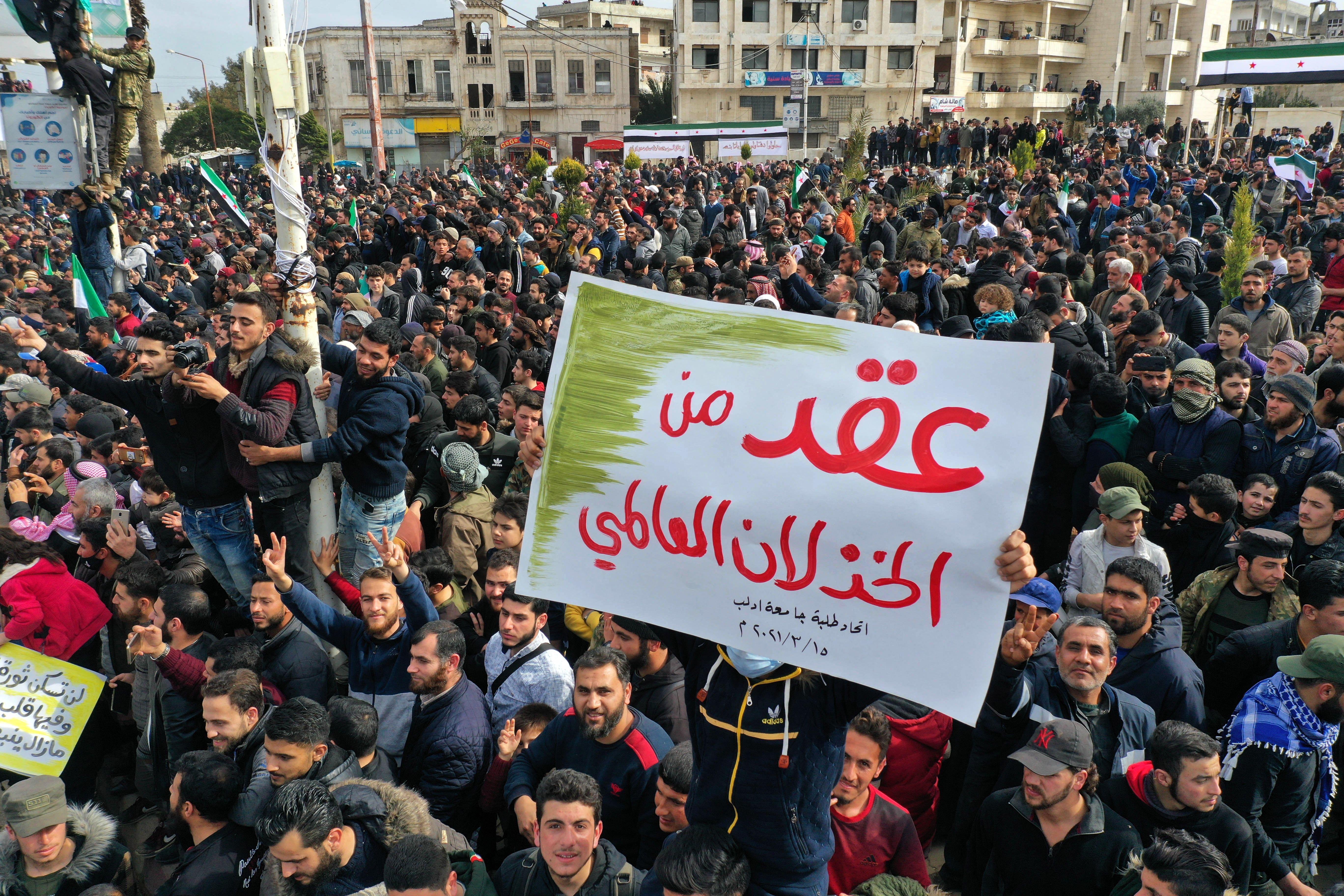 Syrians carrying a placard that reads "A decade of international letdown"