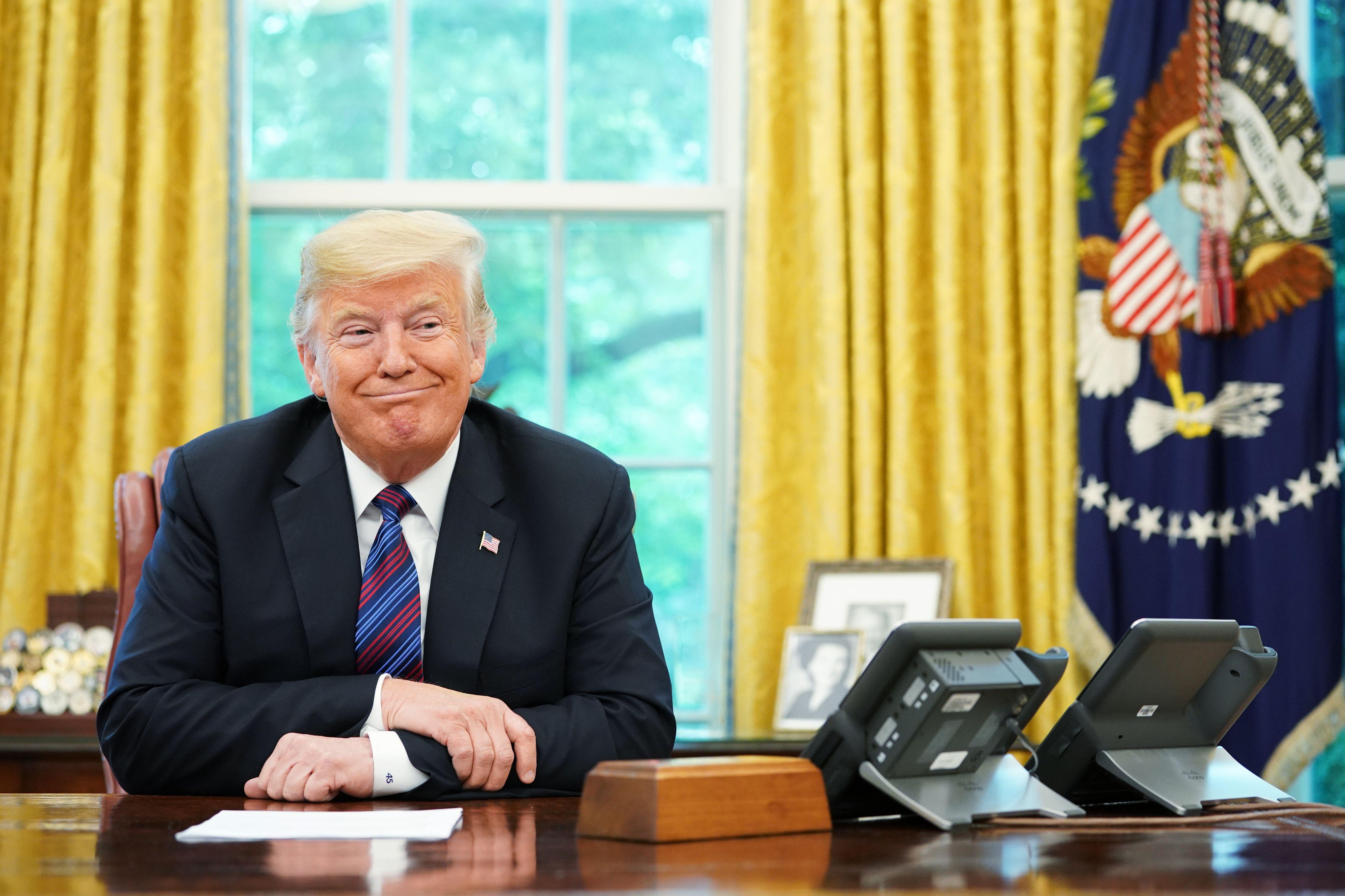 President Trump arms crossed and smirking at his desk in the Oval Office during a phone conversation.