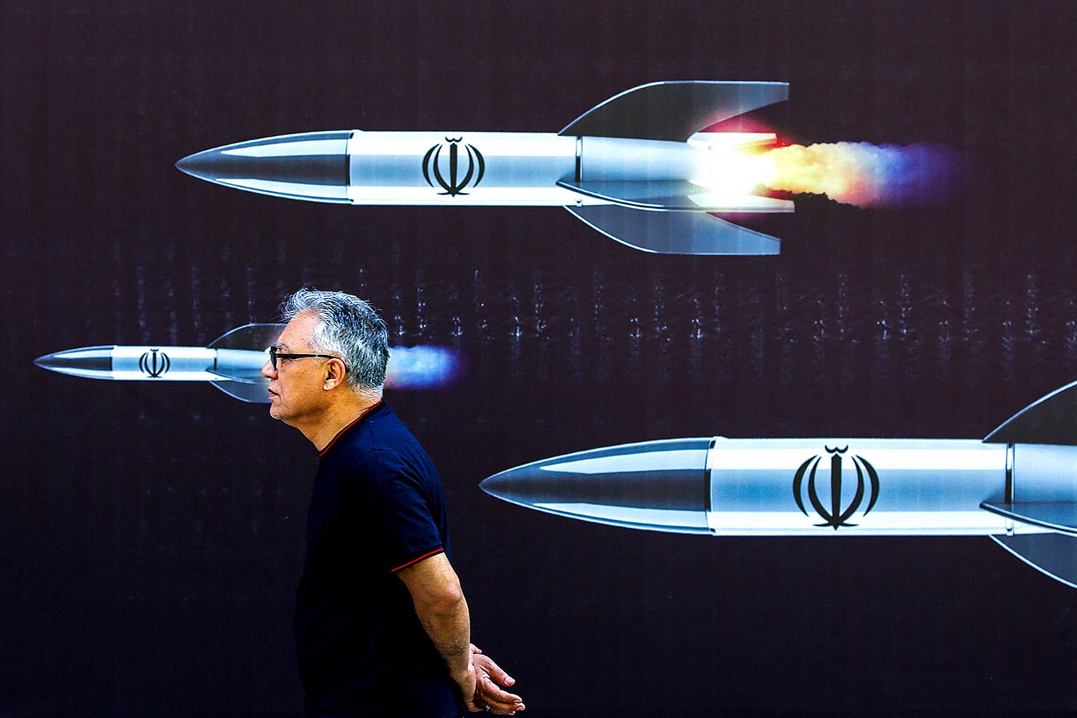 A man walking in front of a poster with missiles on it that takes up the full frame.