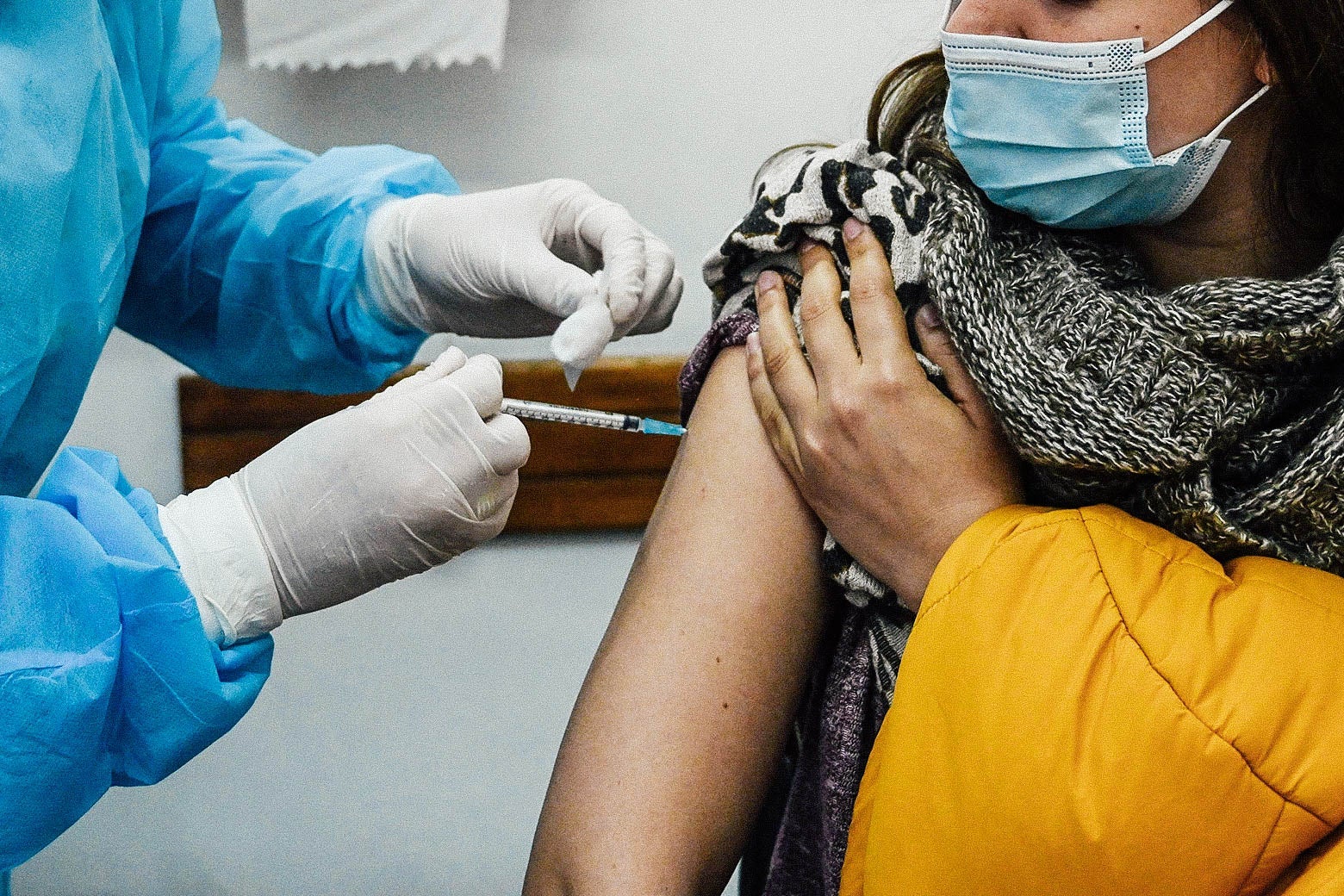 A woman wearing a mask receives a vaccine from a health care worker.