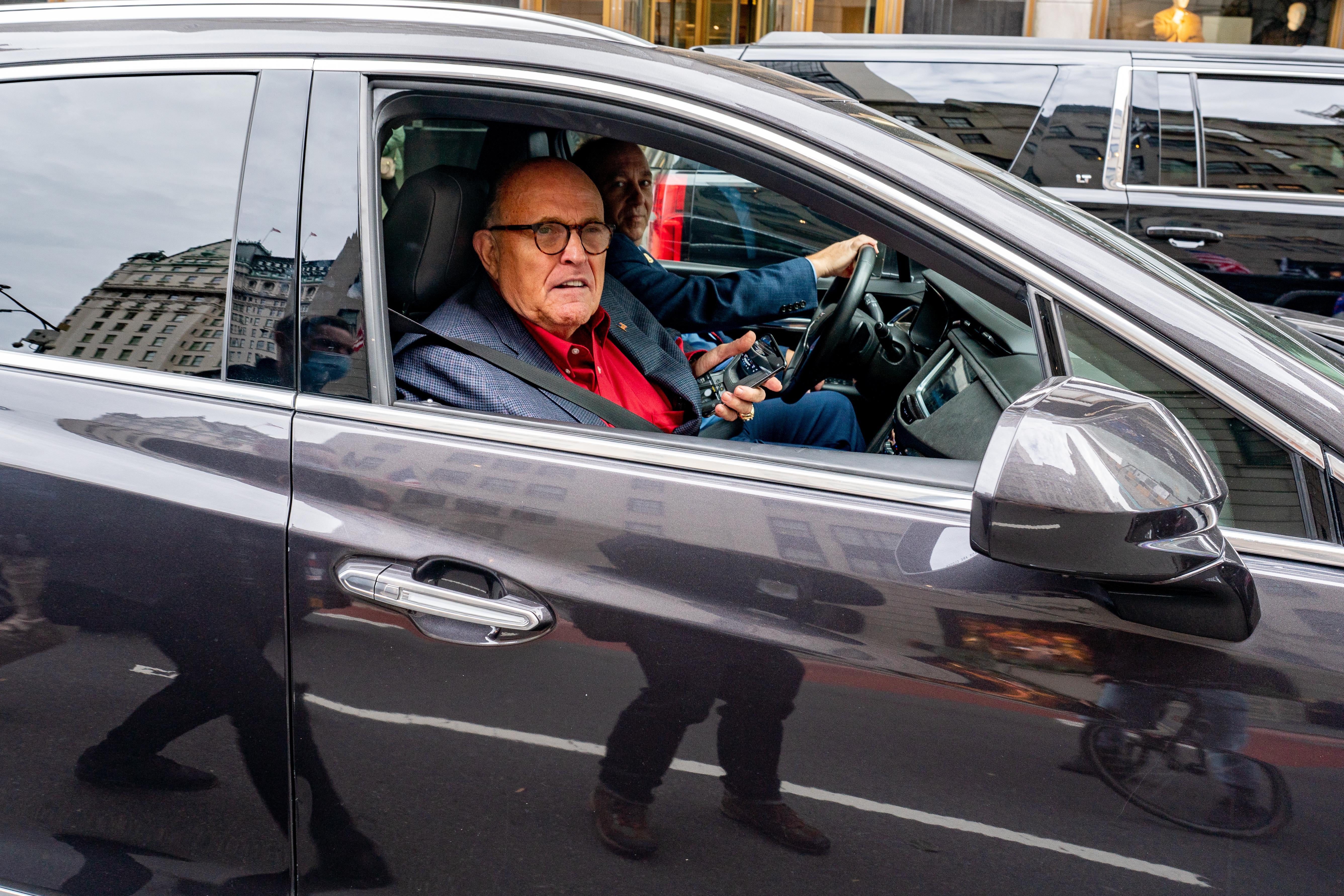 Giuliani holds his phone, sitting in the passenger seat of a black car