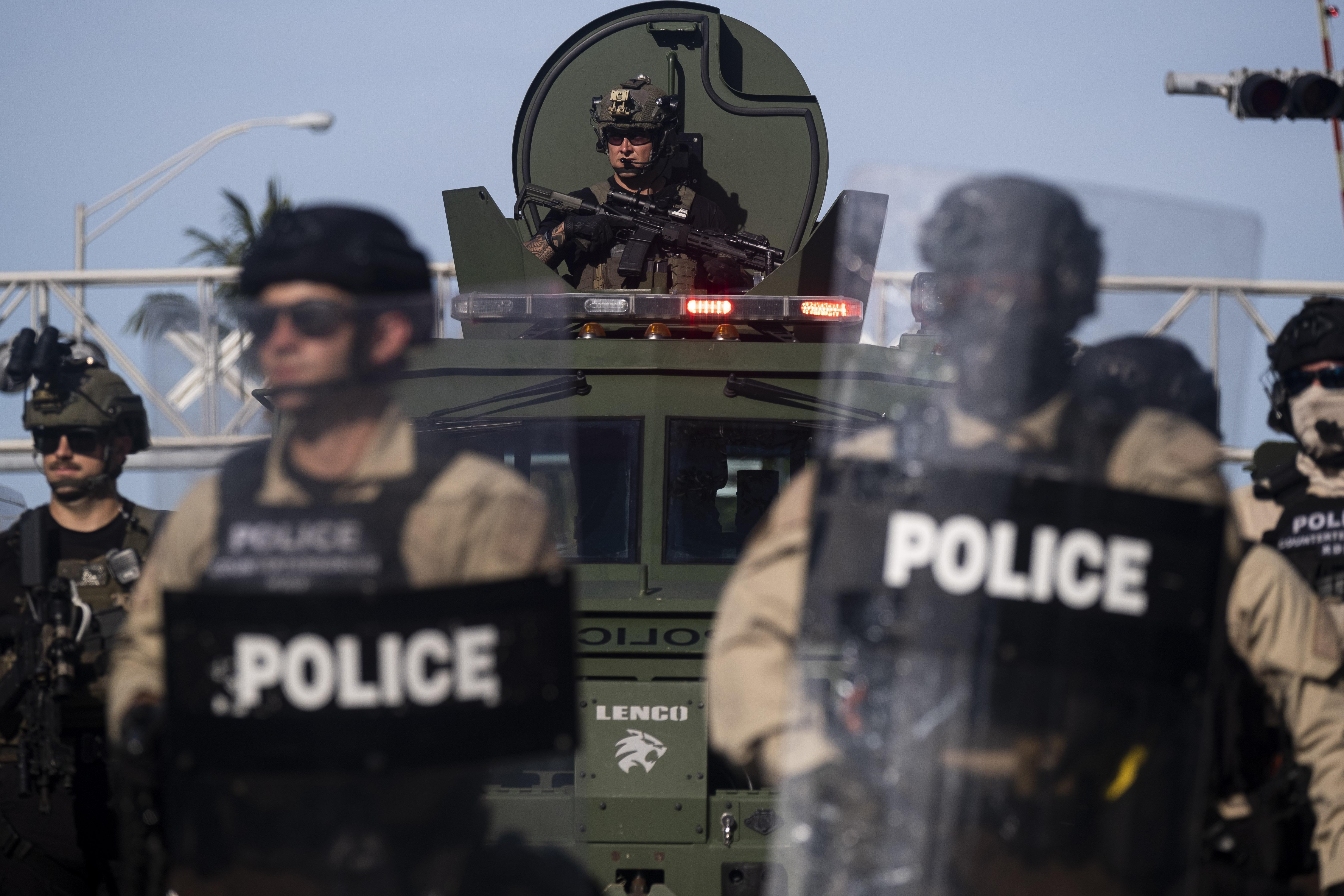 Police in riot gear stand in front of an armored vehicle