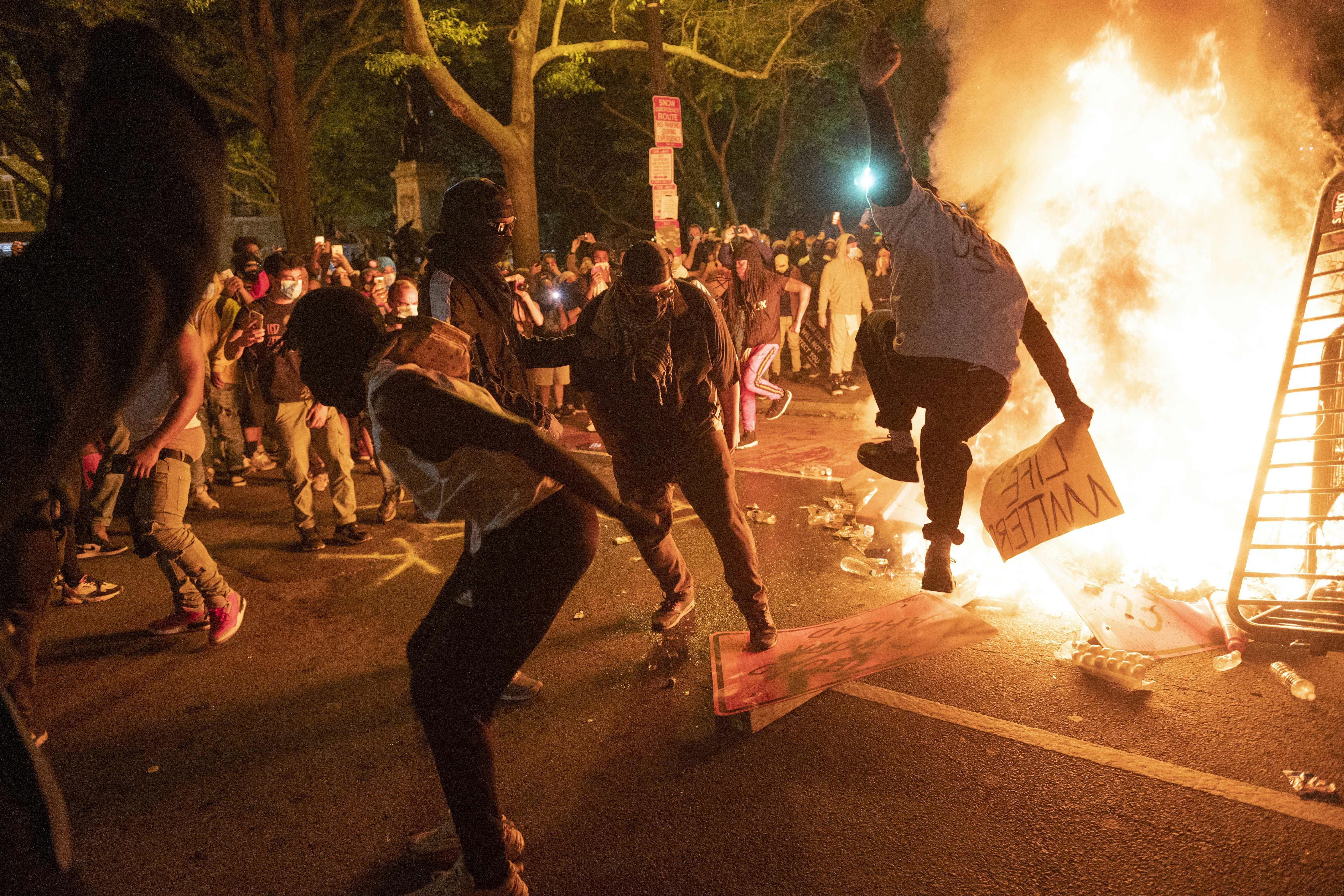 Protesters jump on a street sign near a burning barricade.