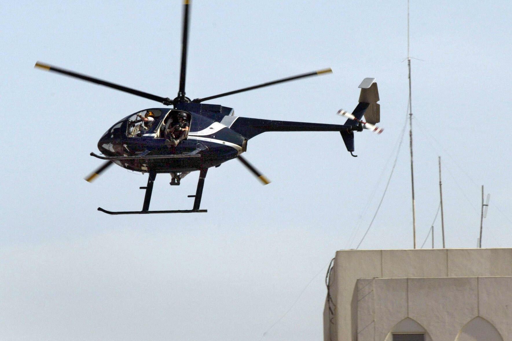 An black helicopter flies over a building. 
