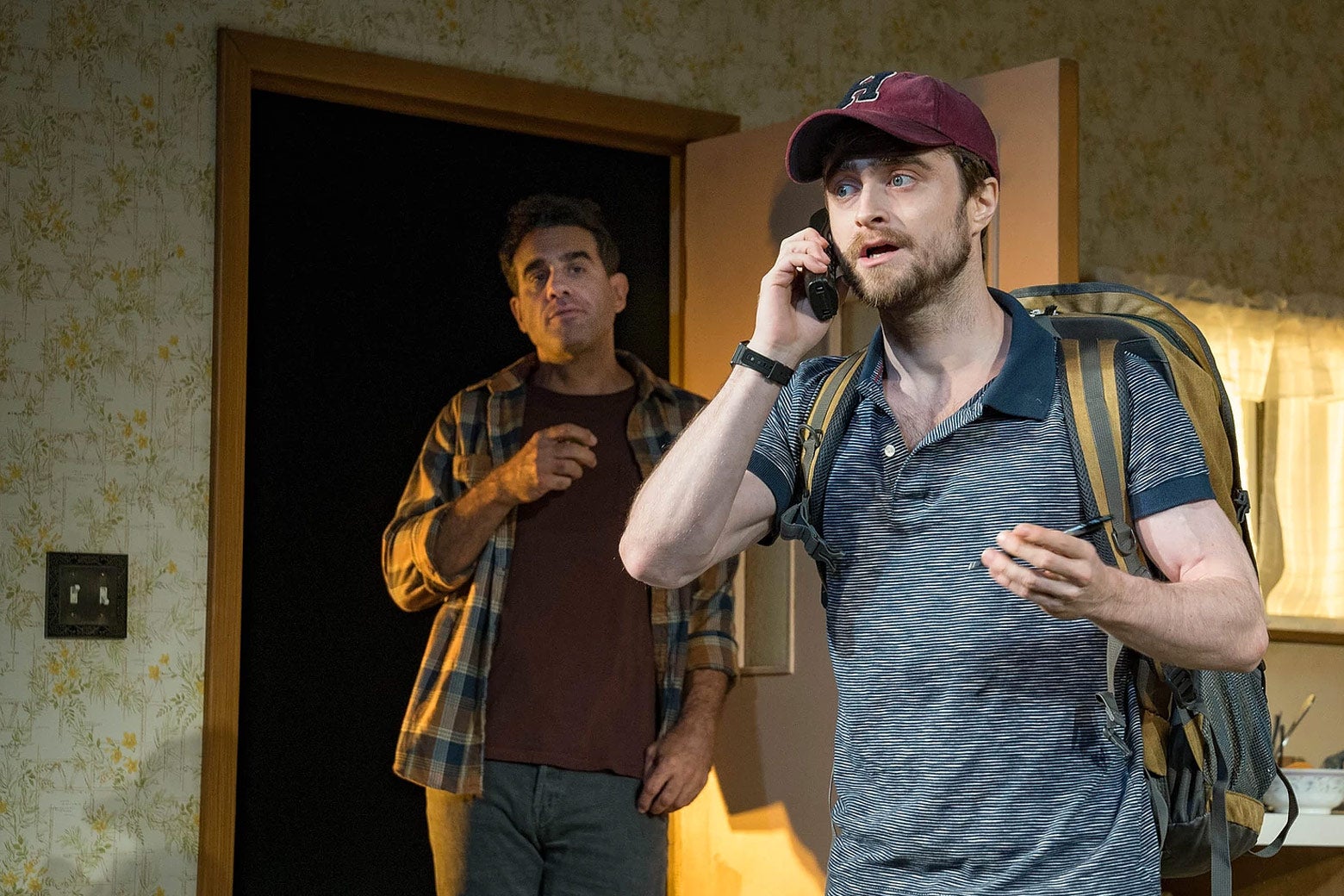 Daniel Radcliffe on the phone with a backpack on. Bobby Cannavale stands in the doorway.