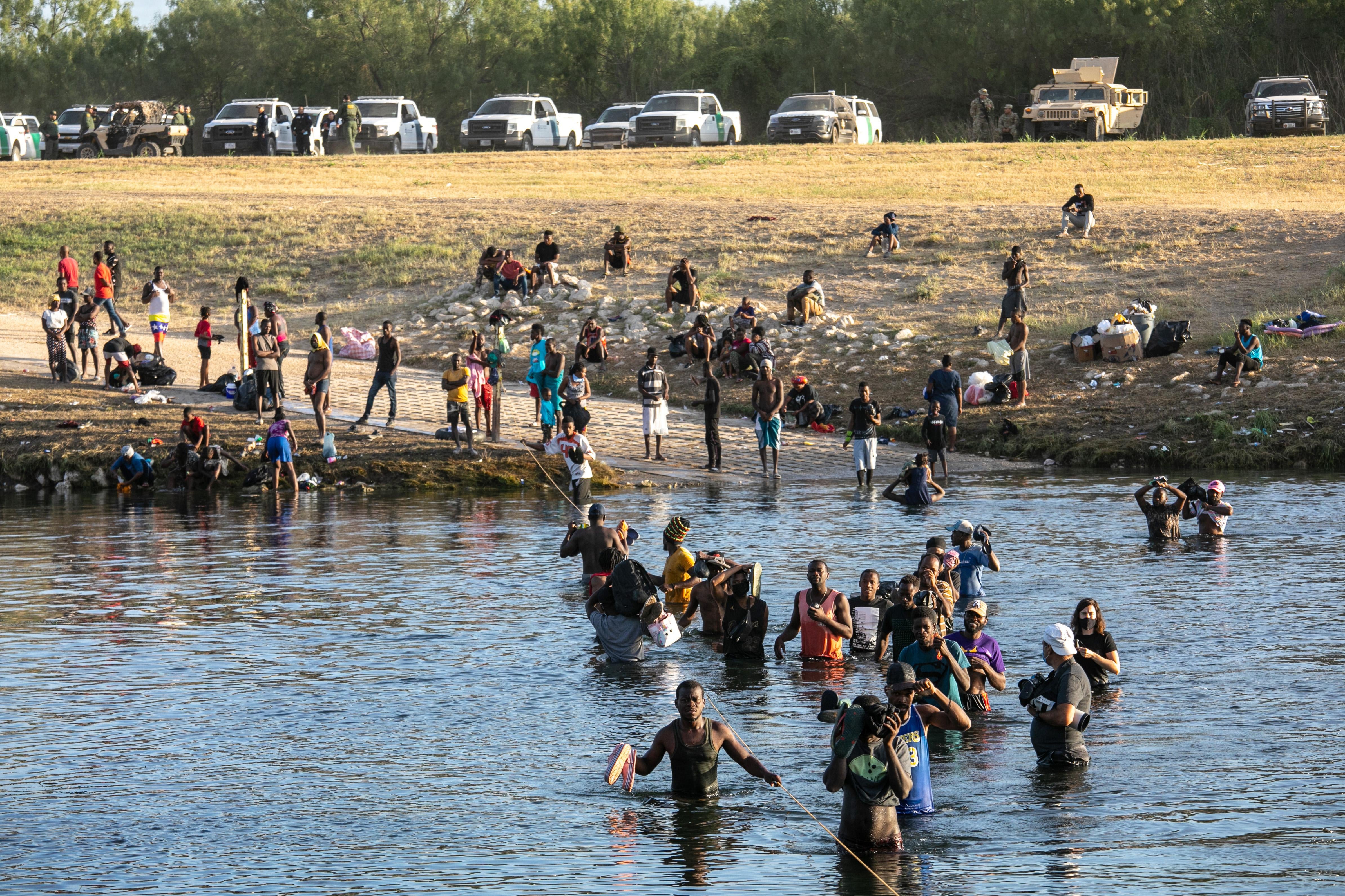 Haitian migrants standing in front of a body of water while others wade through it