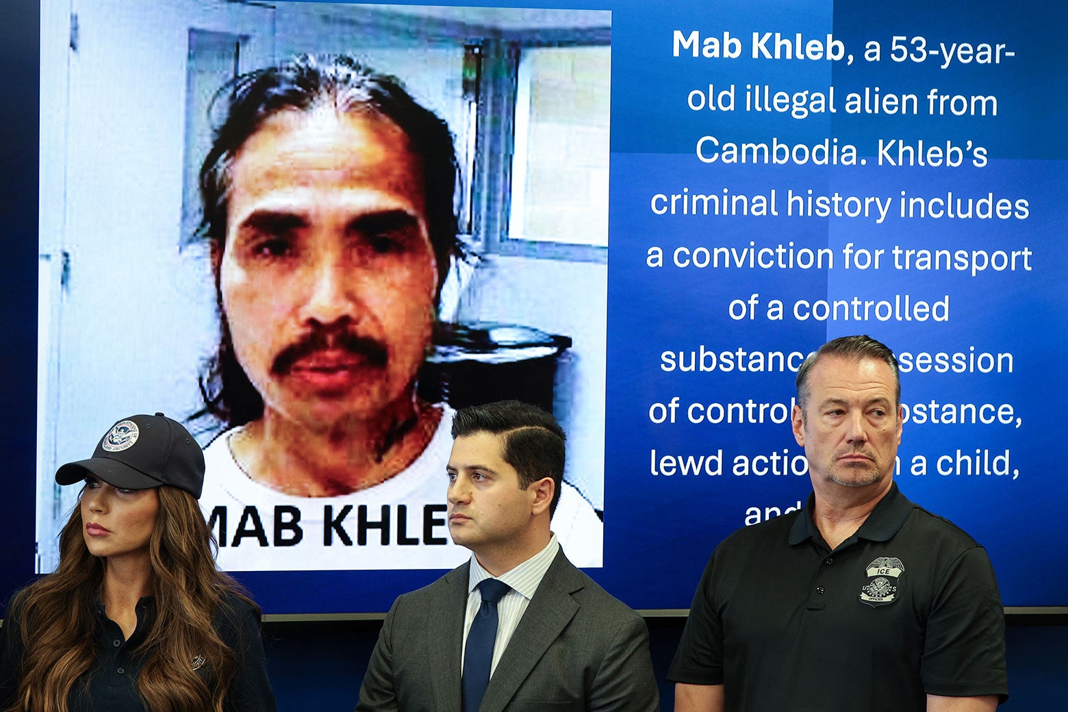 The three officials stand in front of a slide with a photo of Mab Khleb on it.