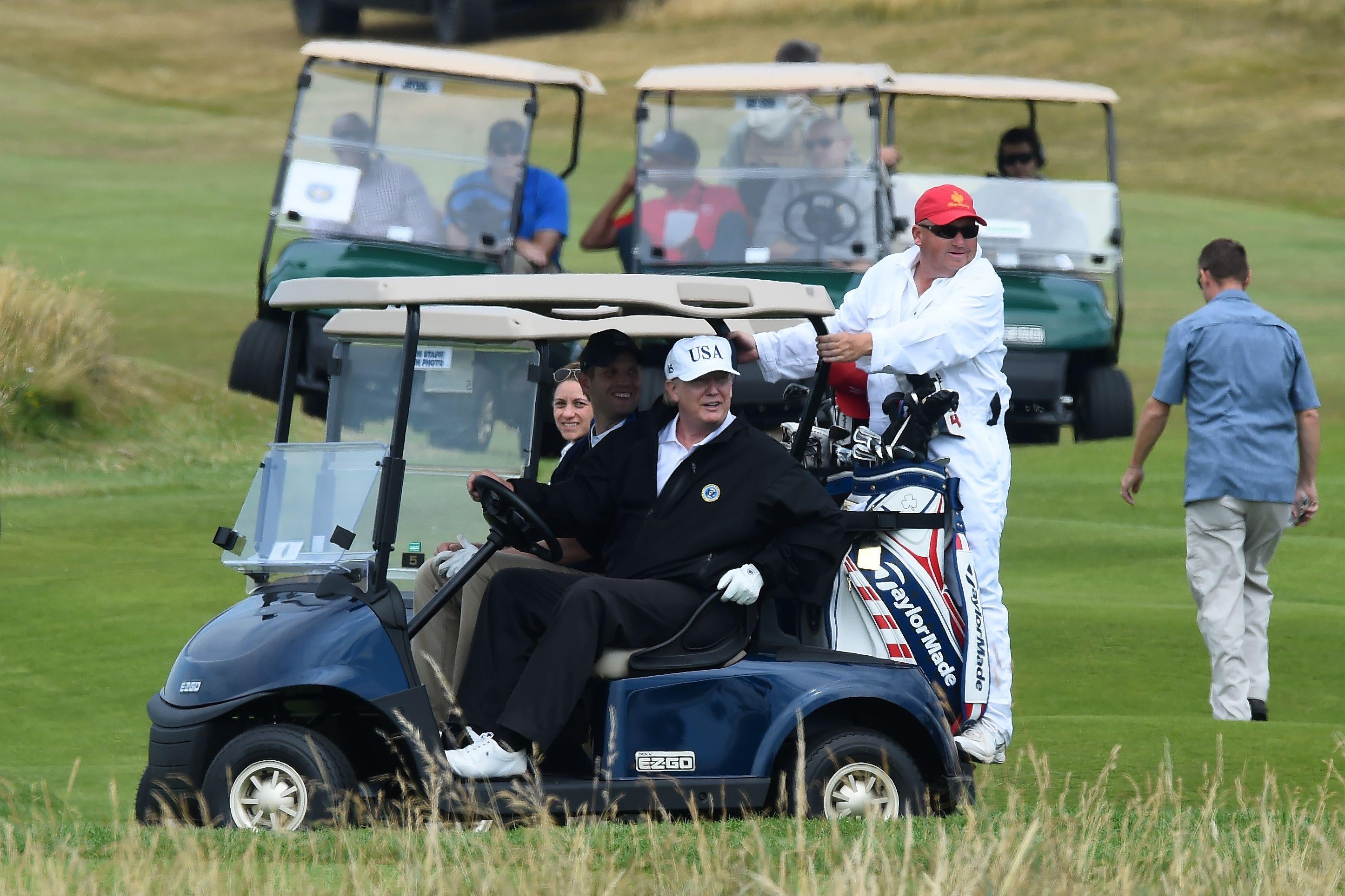 US President Donald Trump (C) sits in a golf cart as he plays a round of golf on the Ailsa course at Trump Turnberry, the luxury golf resort of US President Donald Trump, in Turnberry, southwest of Glasgow, Scotland on July 14, 2018, during the private part of his four-day UK visit. - US President Donald Trump wraps up a four-day visit to Britain, dominated by his blasting of Prime Minister Theresa May's Brexit strategy, by spending the weekend in Scotland. (Photo by ANDY BUCHANAN / AFP)        (Photo credit should read ANDY BUCHANAN/AFP/Getty Images)