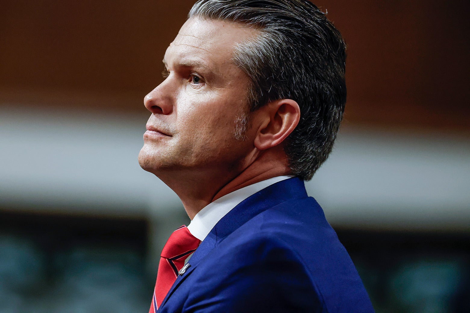 A profile shot of a middle-aged man with salt-and-pepper hair, who wears a blue suit and stares somberly ahead.