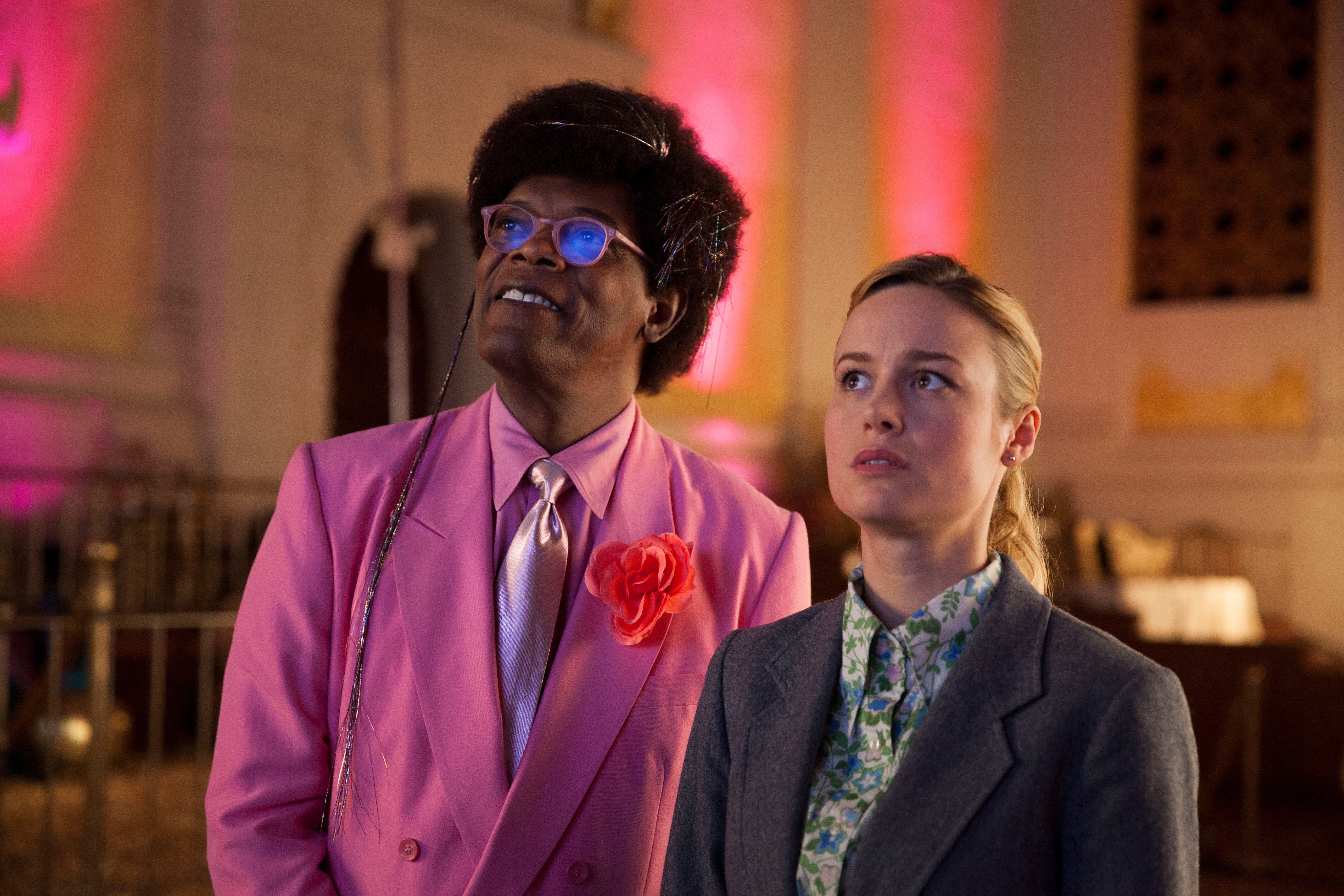 Samuel L Jackson in a pink suit and Brie Larson in a flowered shirt stare off into the distance.