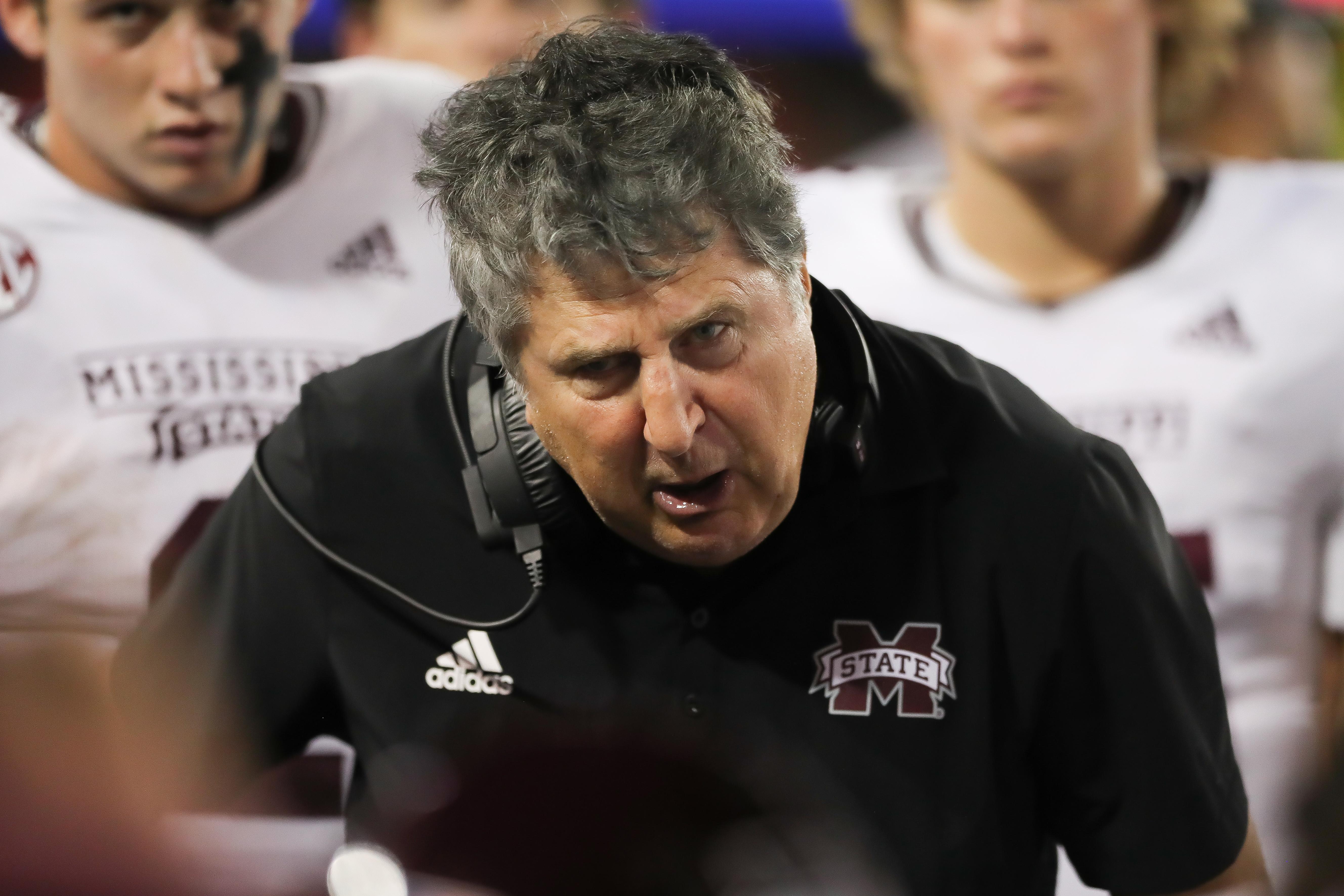 Leach on the sideline, in a headset leaning over and speaking to players