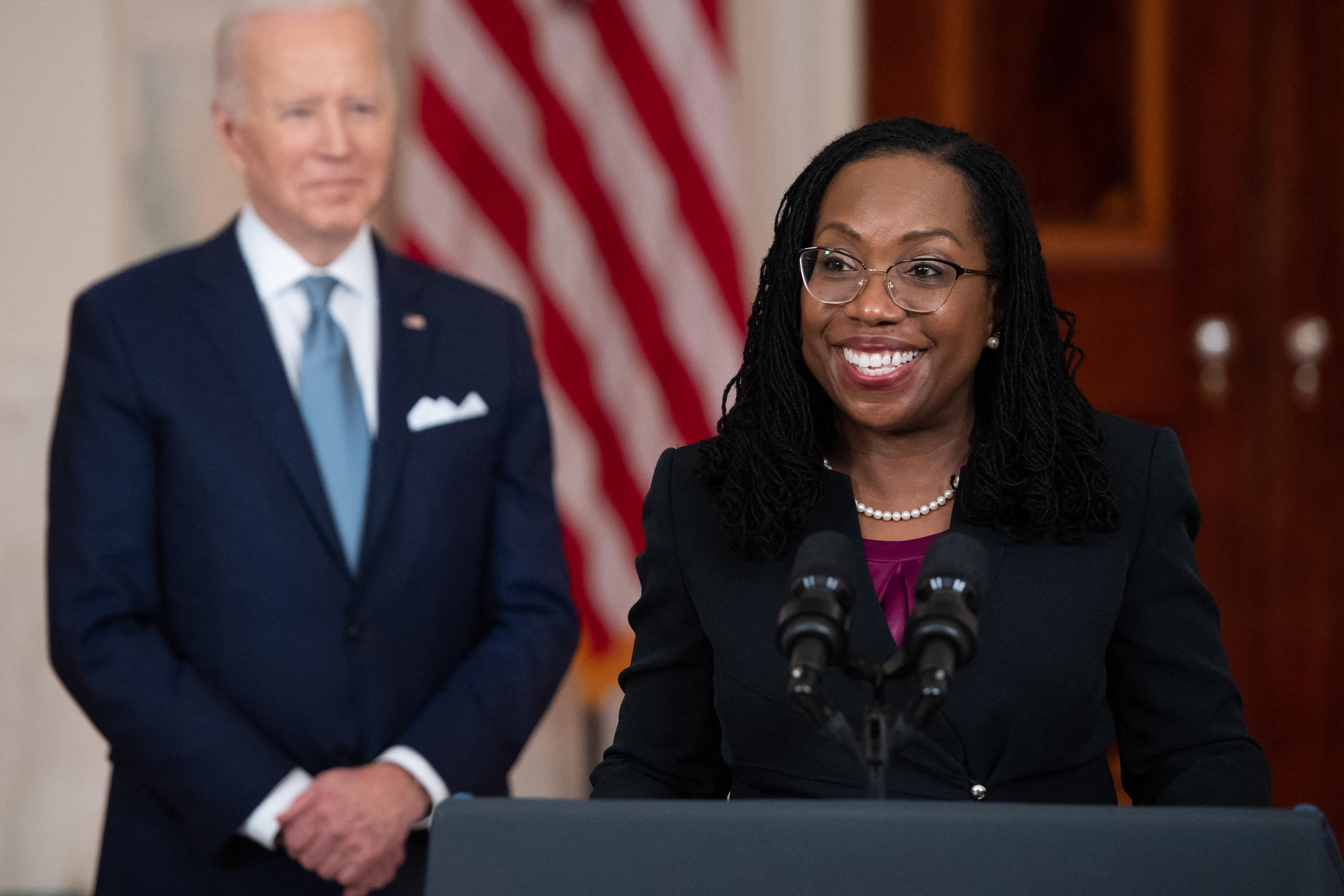 Jackson smiles broadly as she stands at a lectern with Biden smiling behind her