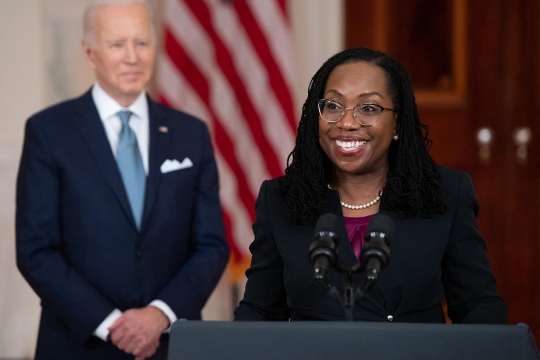 Jackson smiles broadly as she stands at a lectern with Biden smiling behind her