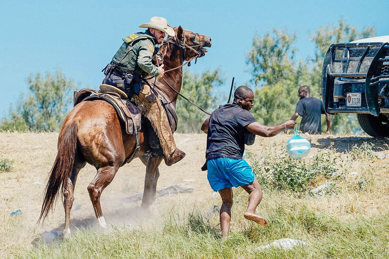 A border patrol agent on horseback chasing and using his reins to try to stop a Haitian migrant, who appears to be running. 