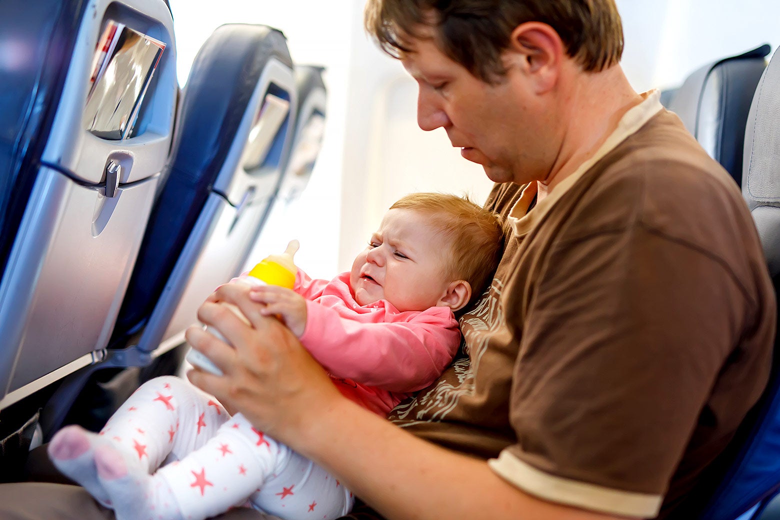 A baby fusses in an airplane seat with his miserable father.