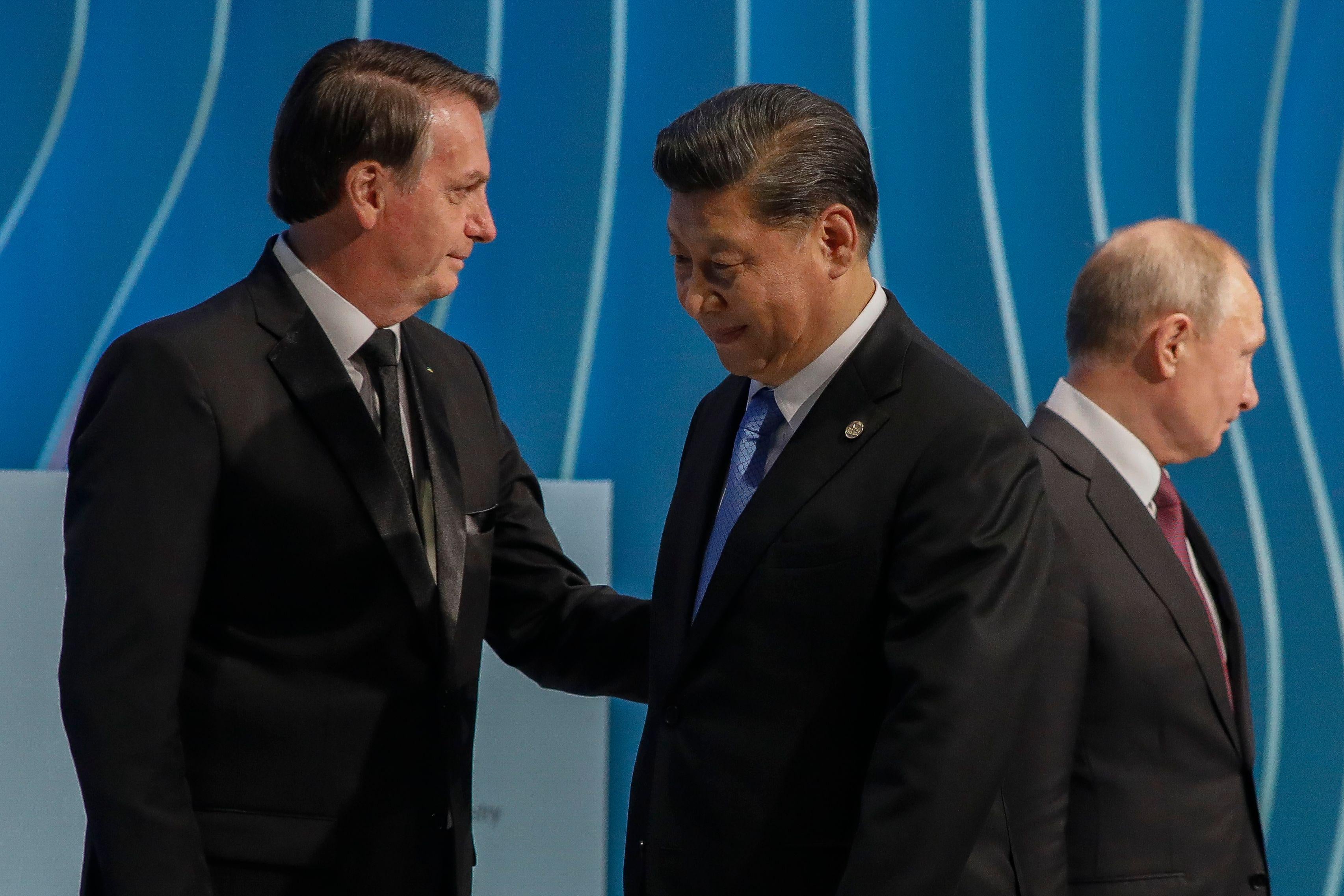 Bolsonaro speaks with Xi. Putin is seen behind them. 