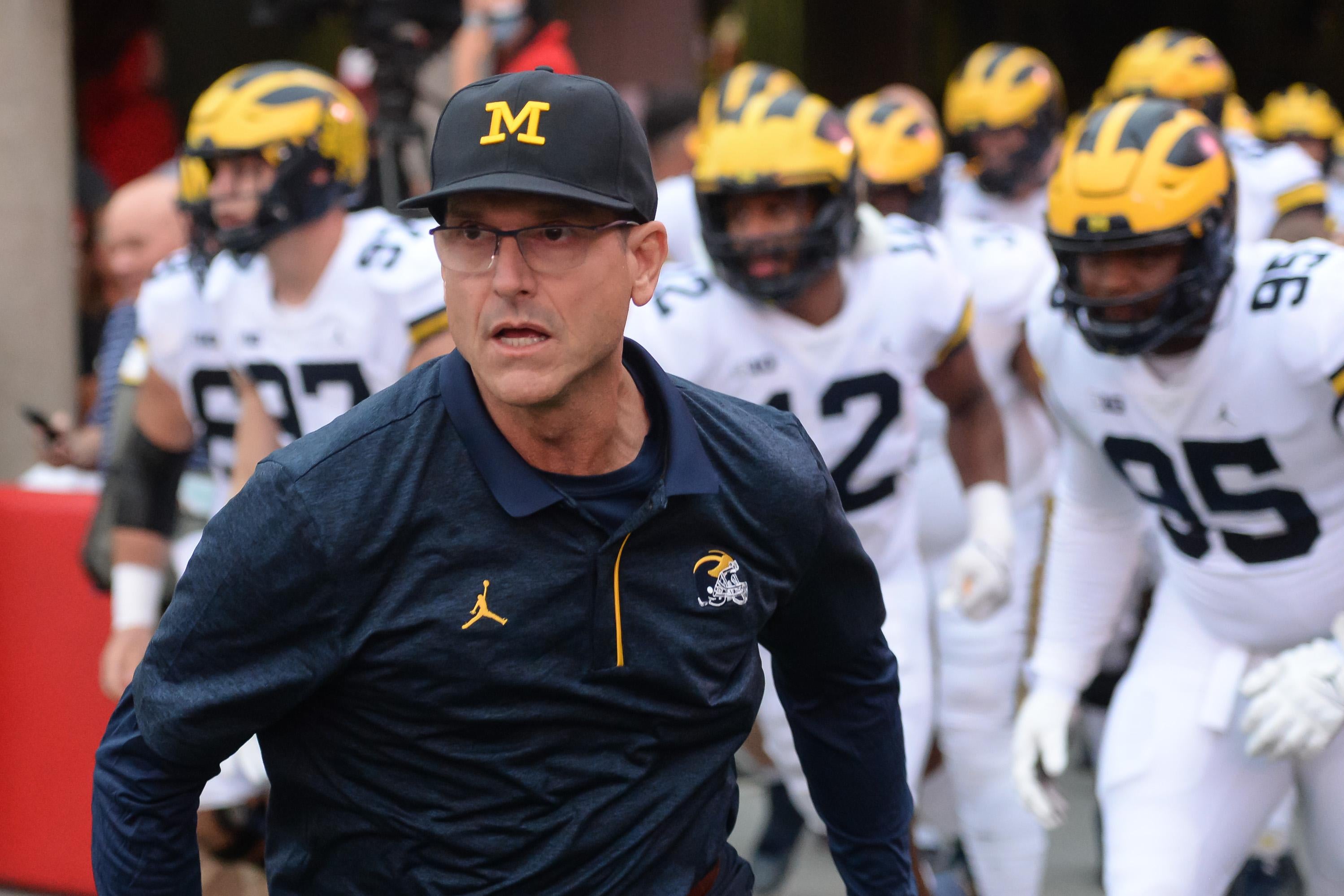 Harbaugh running onto the field with the Michigan players in uniform running behind him