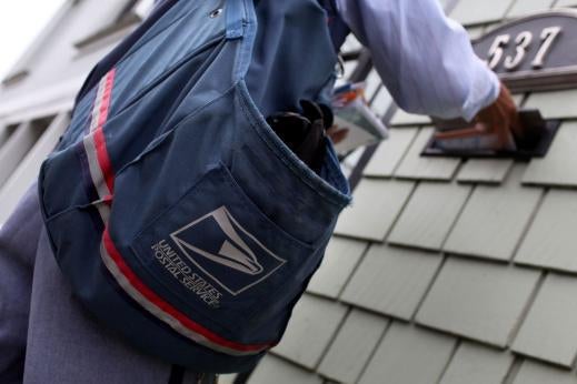 A postal worker with a mailbag inserts letters into a slot.