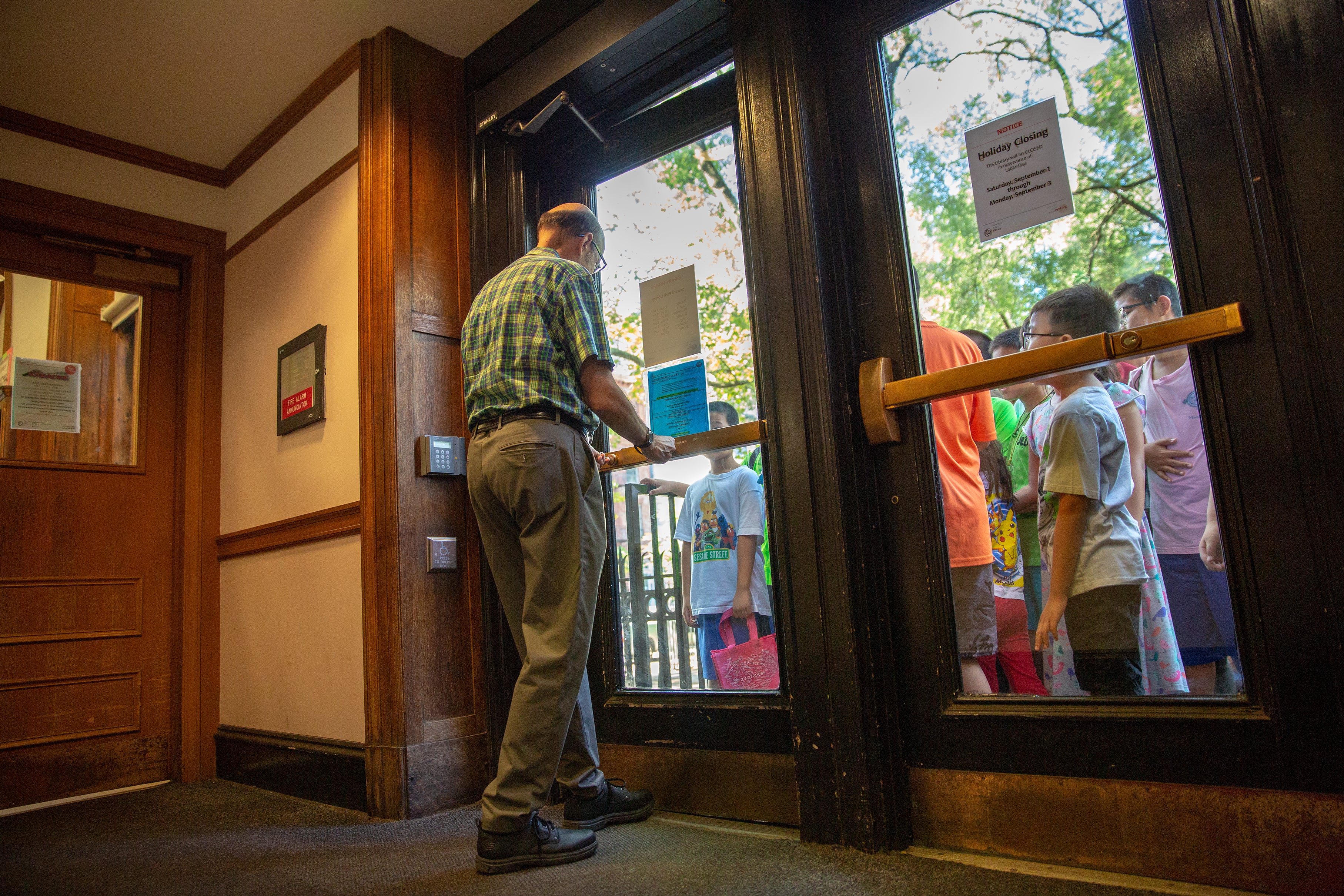 A librarian opens the doors of the library to children waiting outside.