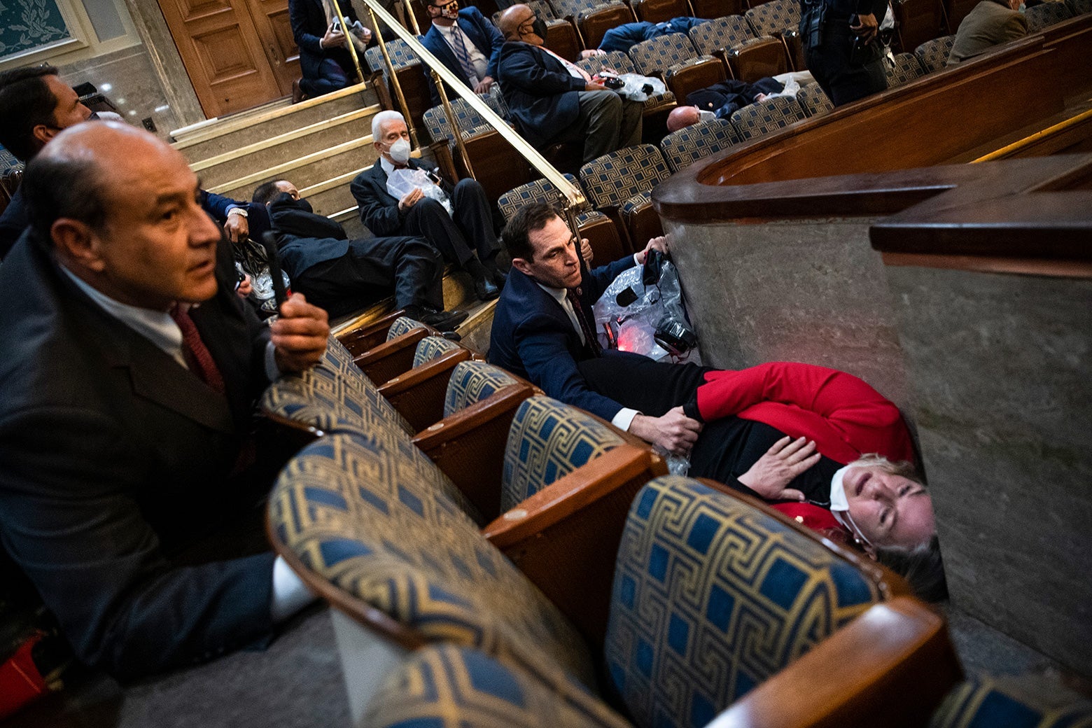 A woman lays on the floor with one hand to her chest and the other holding onto the hand of a man who is crouching down next to her.