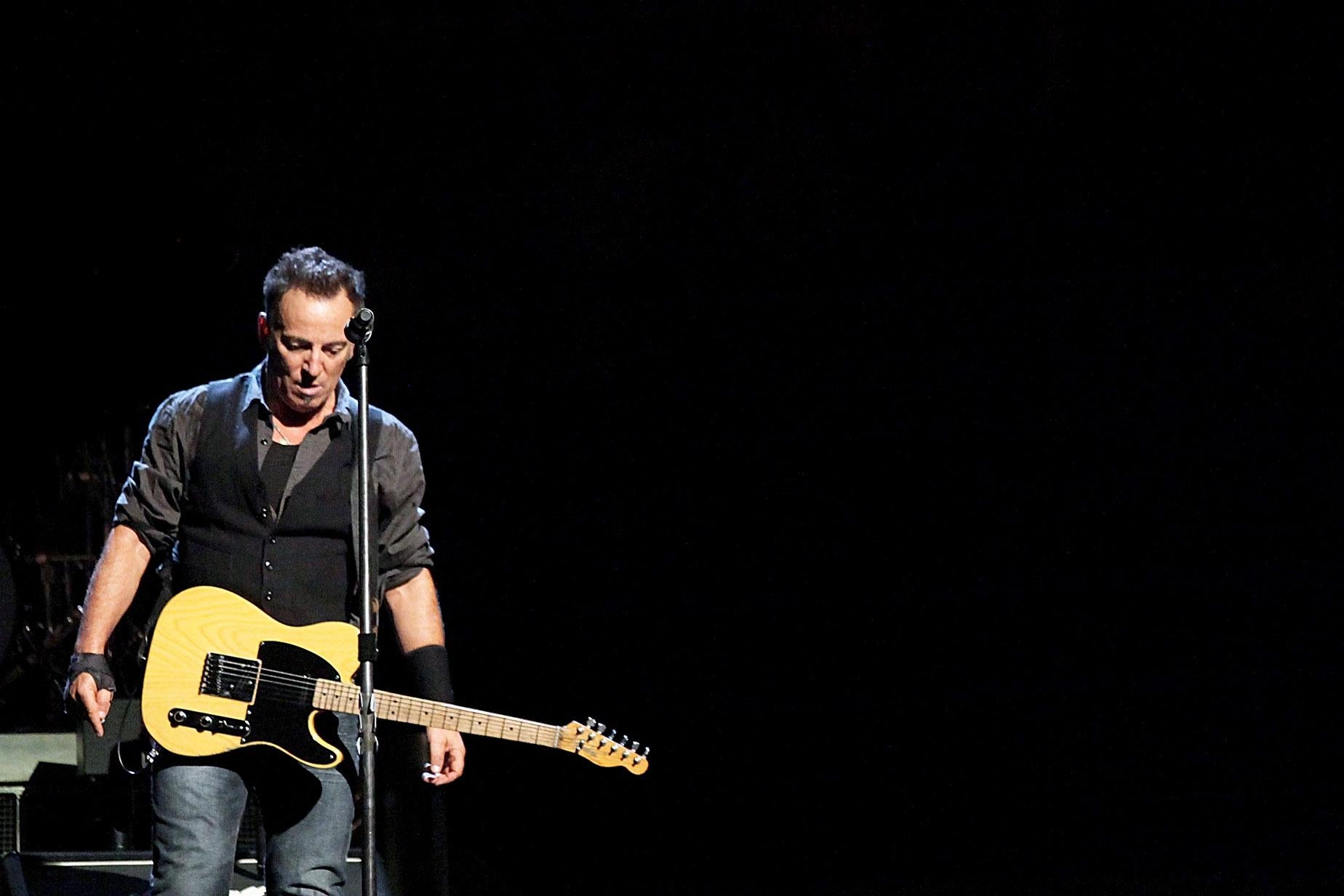Bruce Springsteen onstage with a guitar strapped around him.