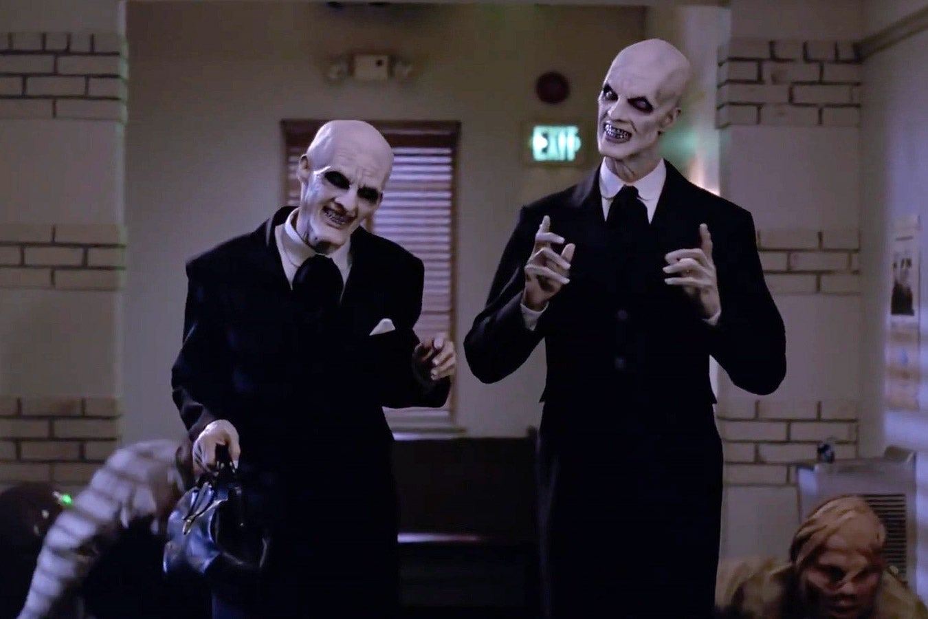 Two vampire-looking monsters bare their teeth and wear suits.