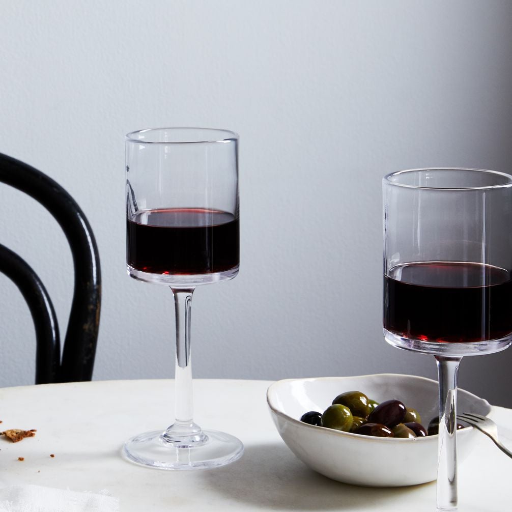 Two glasses of red wine sit beside a bowl of olives and a plate of cheese and crackers on a table