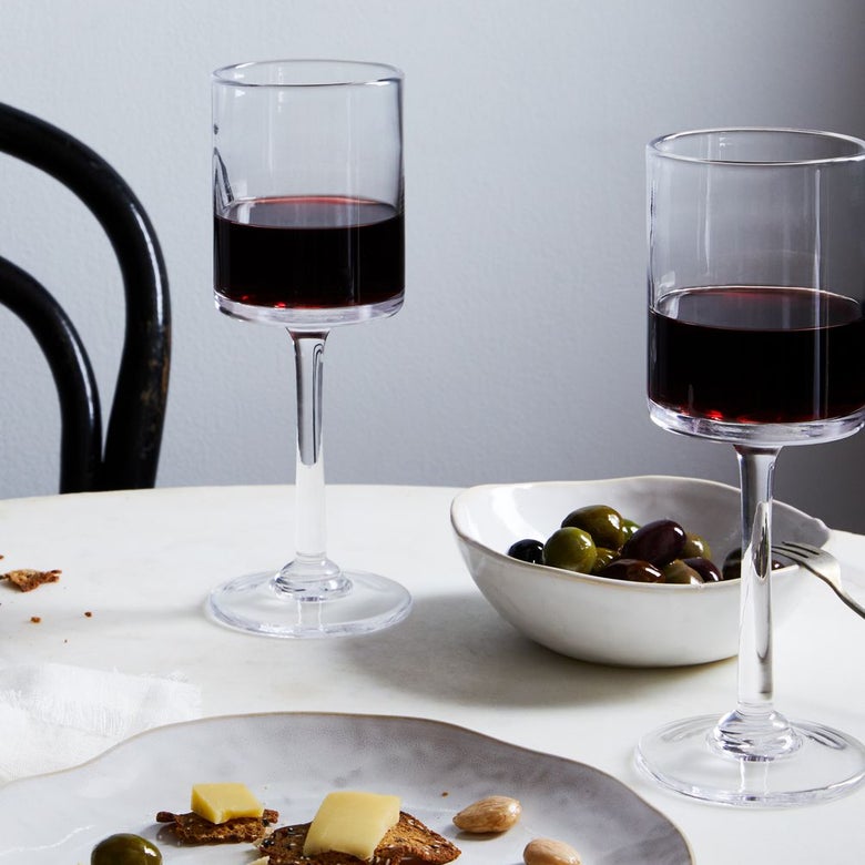 Two glasses of red wine sit beside a bowl of olives and a plate of cheese and crackers on a table