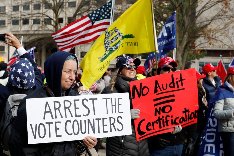 A crowd of pro-Trump protesters. One person holds a sign that reads "Arrest the Vote Counters." Another holds a sign that reads "No Audit = No Certification."