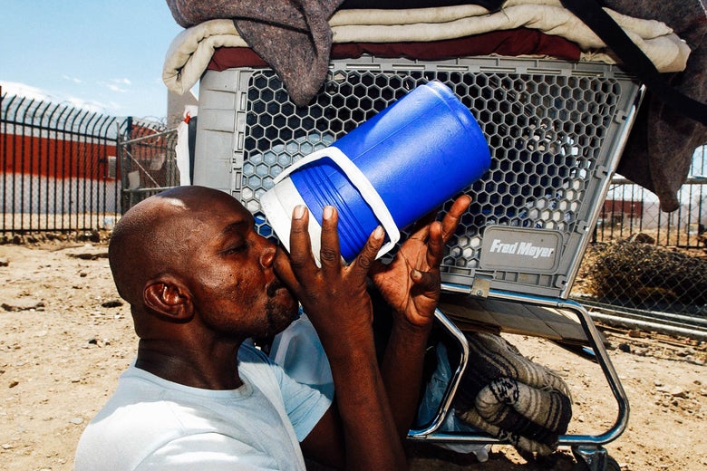 Desmont Smith, who is homeless, sit in the shade of his shopping cart drinking water, near the train tracks in Phoenix where the temperature reached 108 degrees.