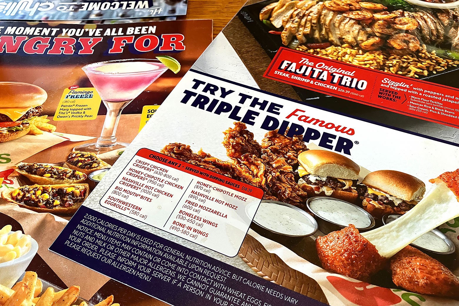 A spread of menus on a Chili's table that spotlights the Triple Dipper, fajitas, and a Flamingo Freeze frozen margarita.