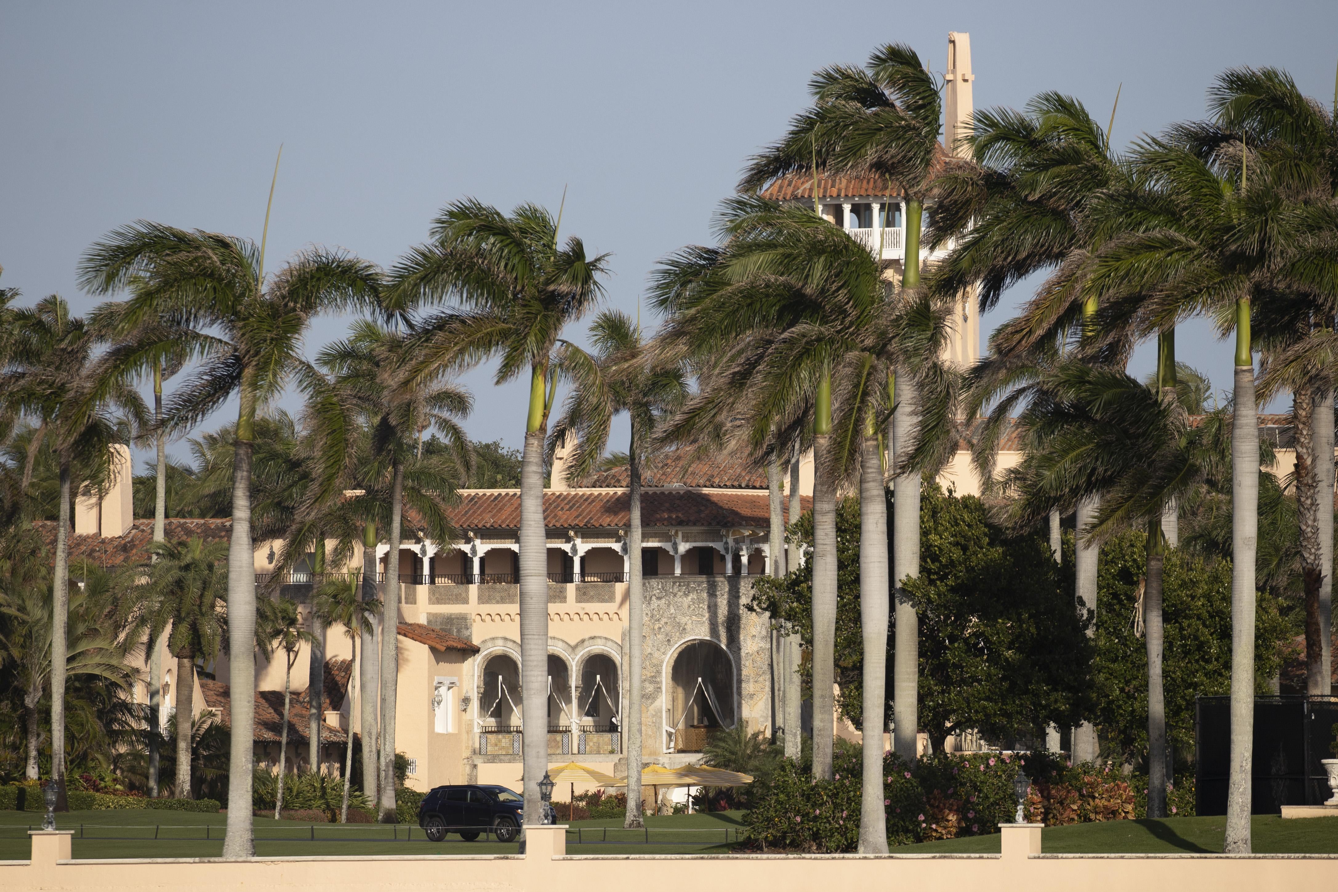 A Spanish-style villa building, in a manicured lawn, with palm trees blowing in the wind.
