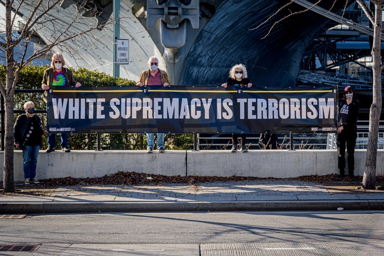 People stand at a highway overpass holding up a sign that says "White Supremacy Is Terrorism"
