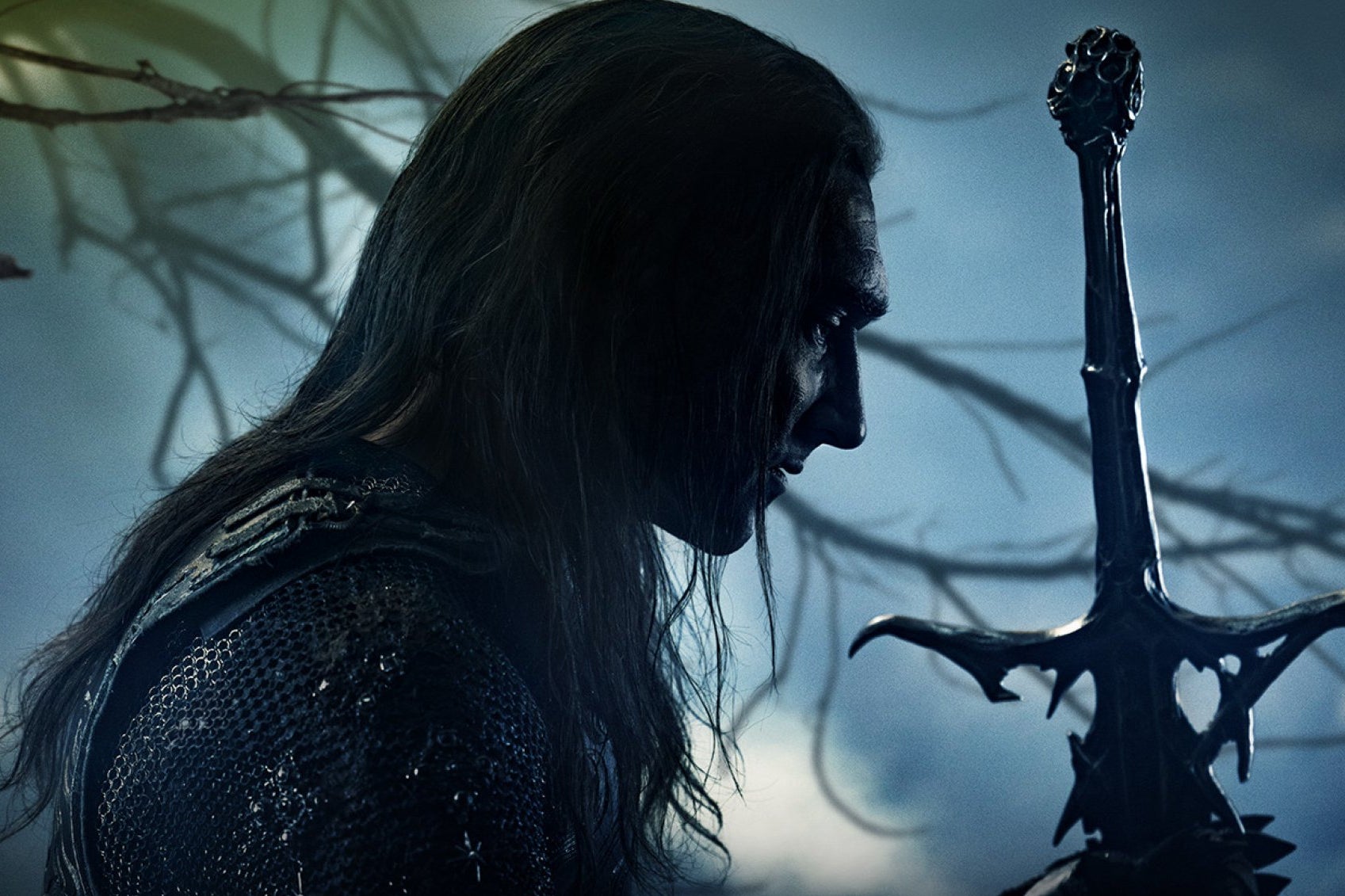 A man with long black hair is seen in profile, facing the hilt of a sword in his hand.