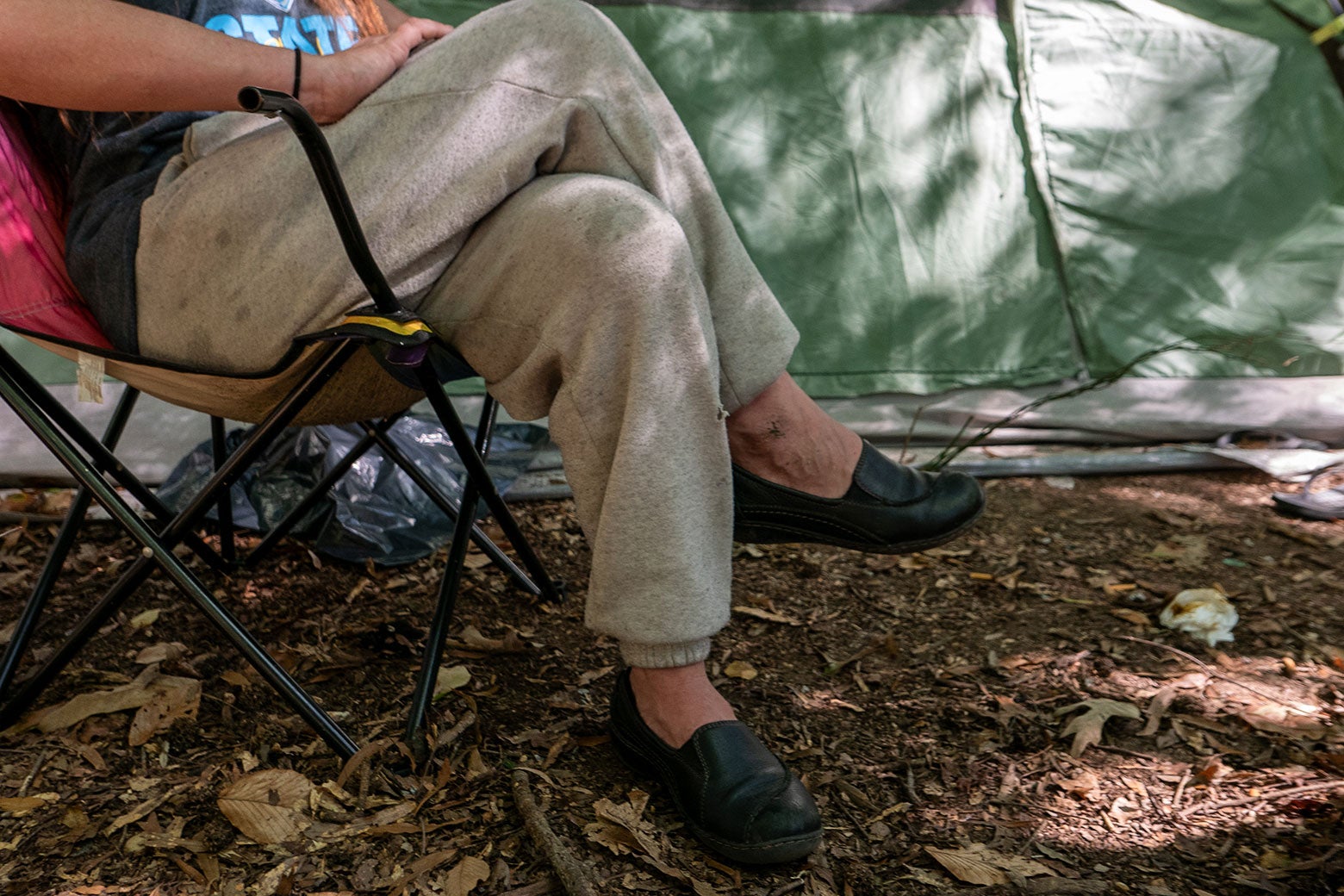 In a remote part of the D.C. woods, Meghann Abraham sits in a camping chair beside her tent.