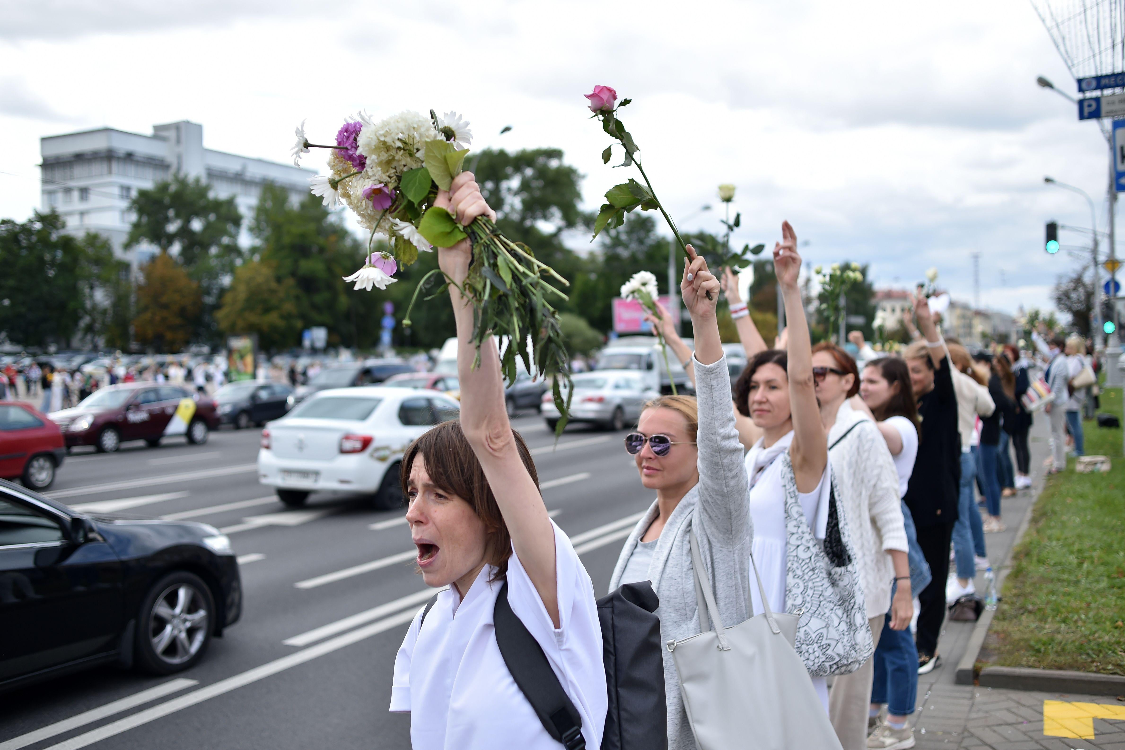 Women wearing white chant slogans as they stand along the side of the street in Minsk. 