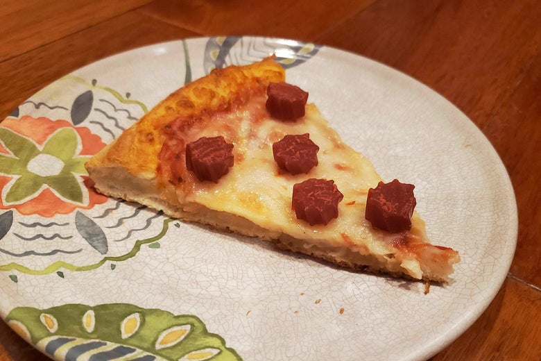 A slice of cheese pizza on a plate with slices of red licorice on top.