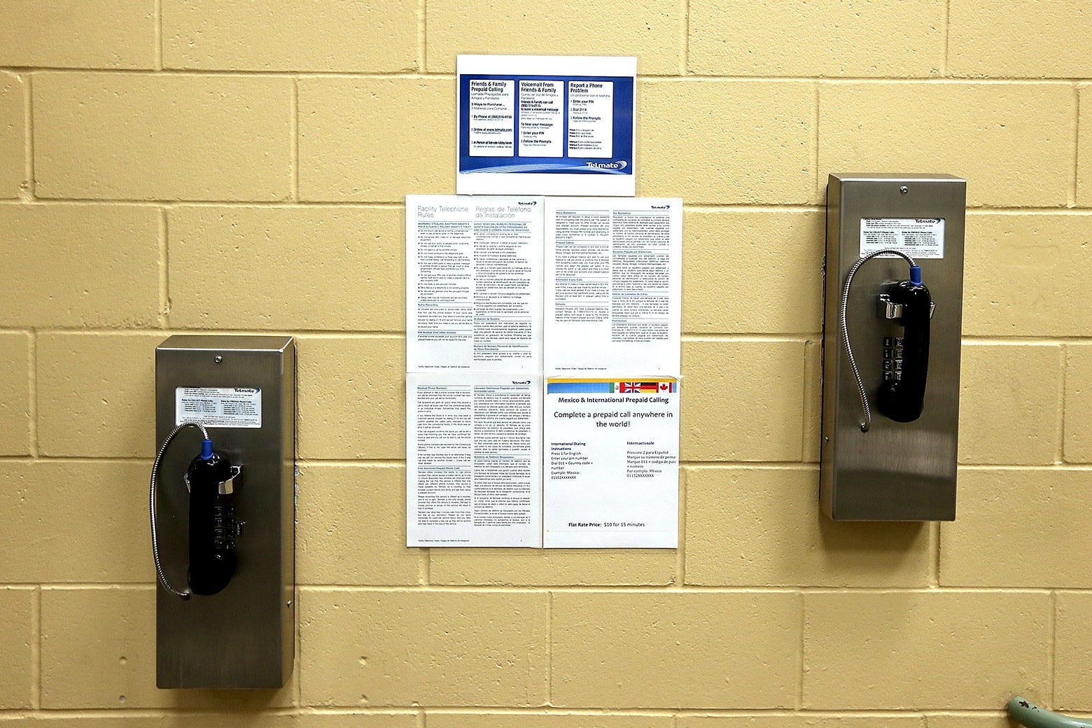 Two staggered pay phones attached to a brick wall.