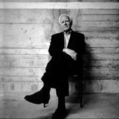 Author John Le Carré sitting in a chair against a wood paneled wall.
