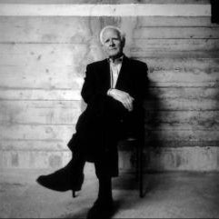 Author John Le Carré sitting in a chair against a wood paneled wall.