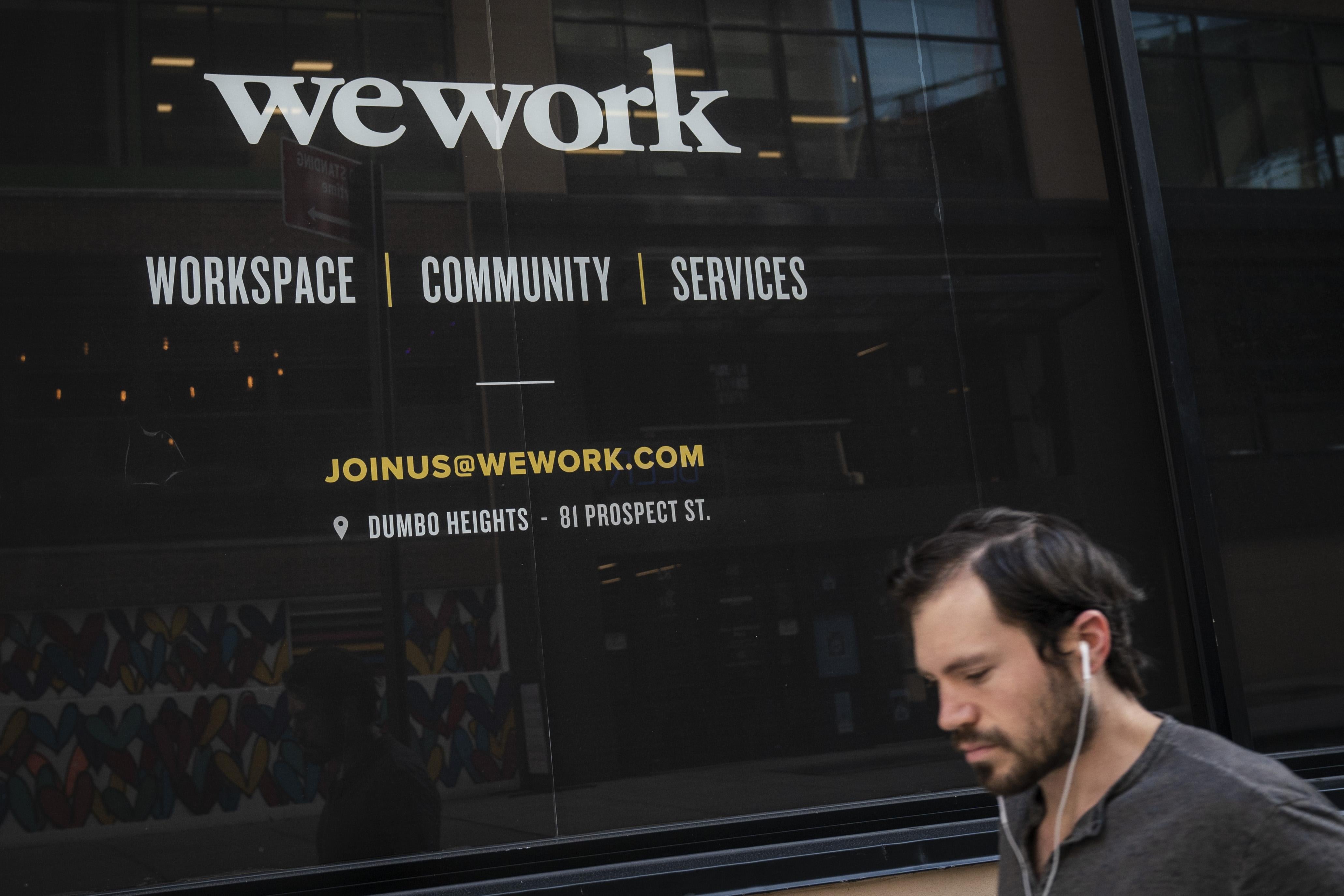 A man with earbuds in walks by the façade of a WeWork building