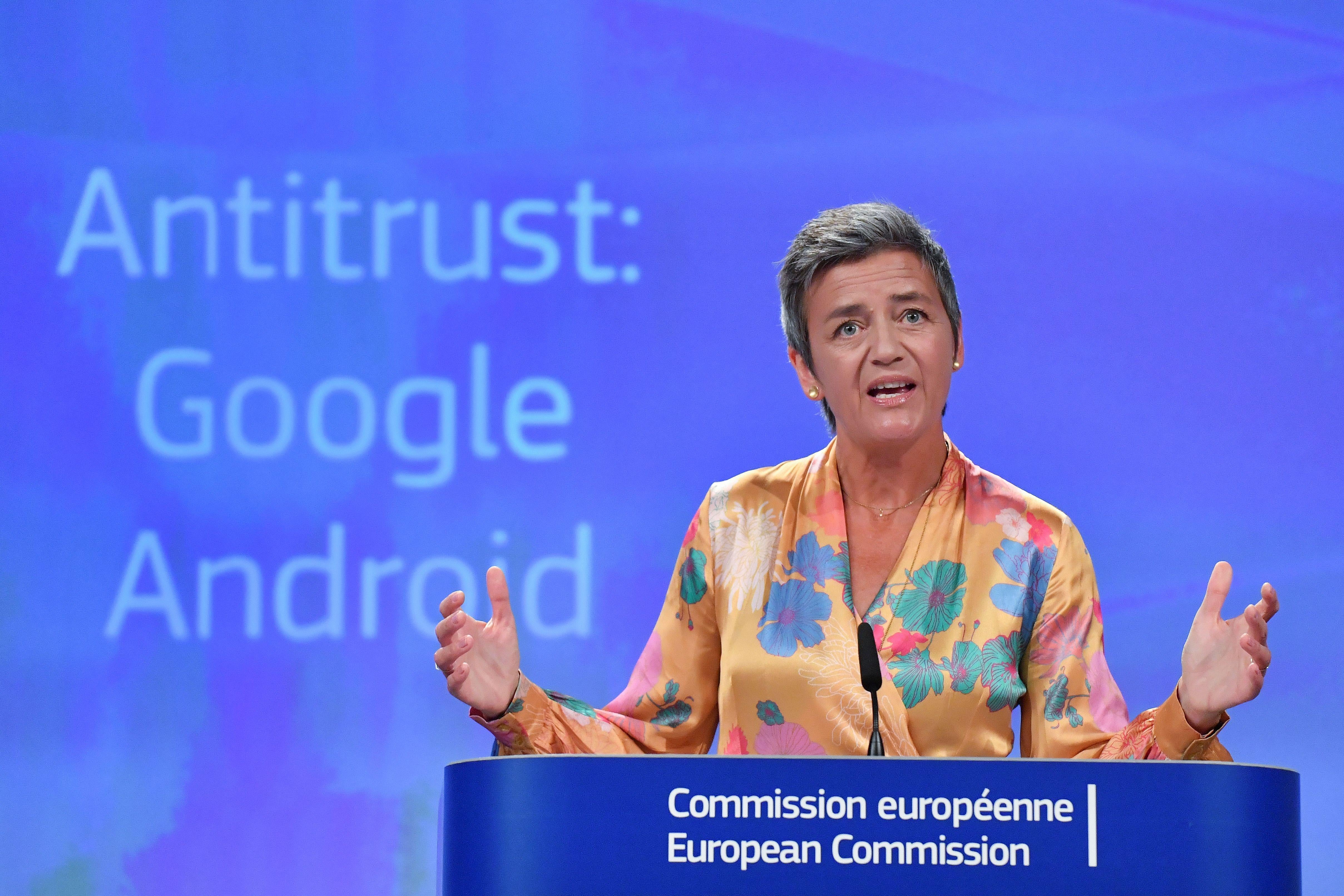 Margrethe Vestager stands at a podium with the words "Antitrust: Google Android" behind her.