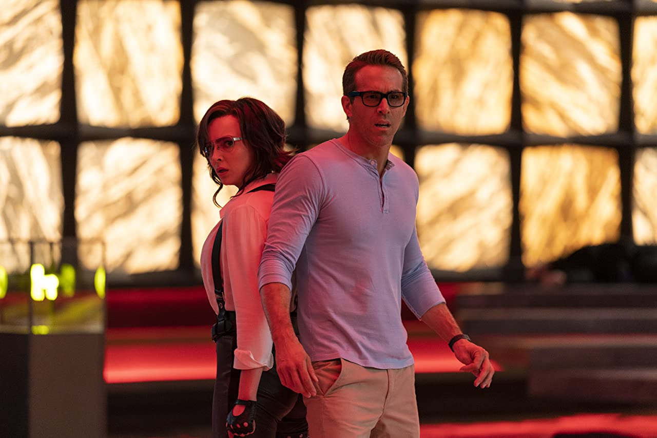 Jodi Comer and Ryan Reynolds stand back to back in a futuristic room in a still from Free Guy.